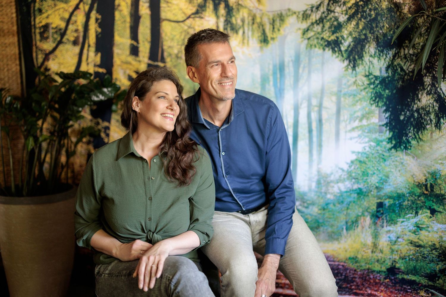 Smiling couple sitting together in front of lush forest nature backdrop indoors.