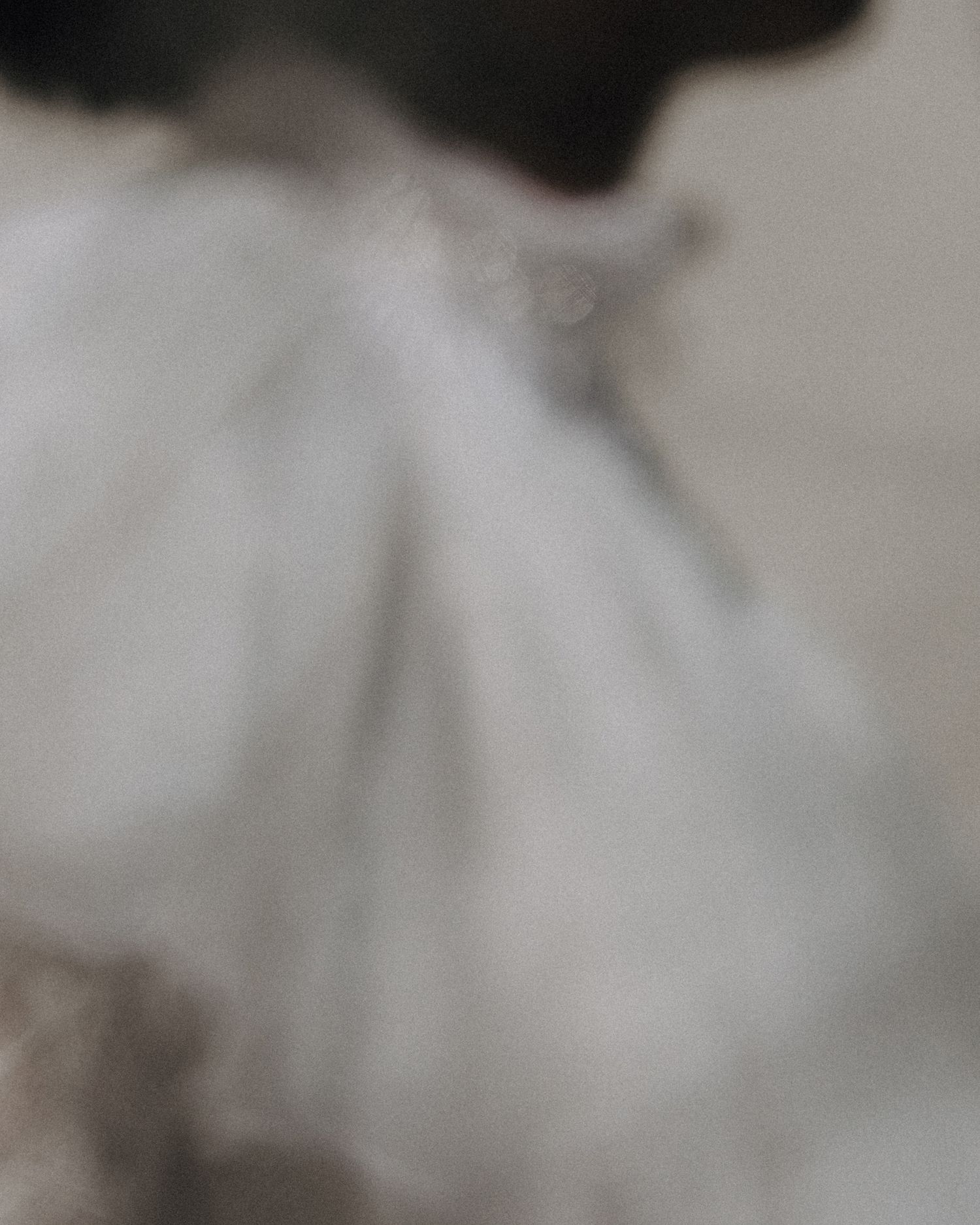 Soft blurred abstract close-up of white ruffled fabric with dark hair detail above.