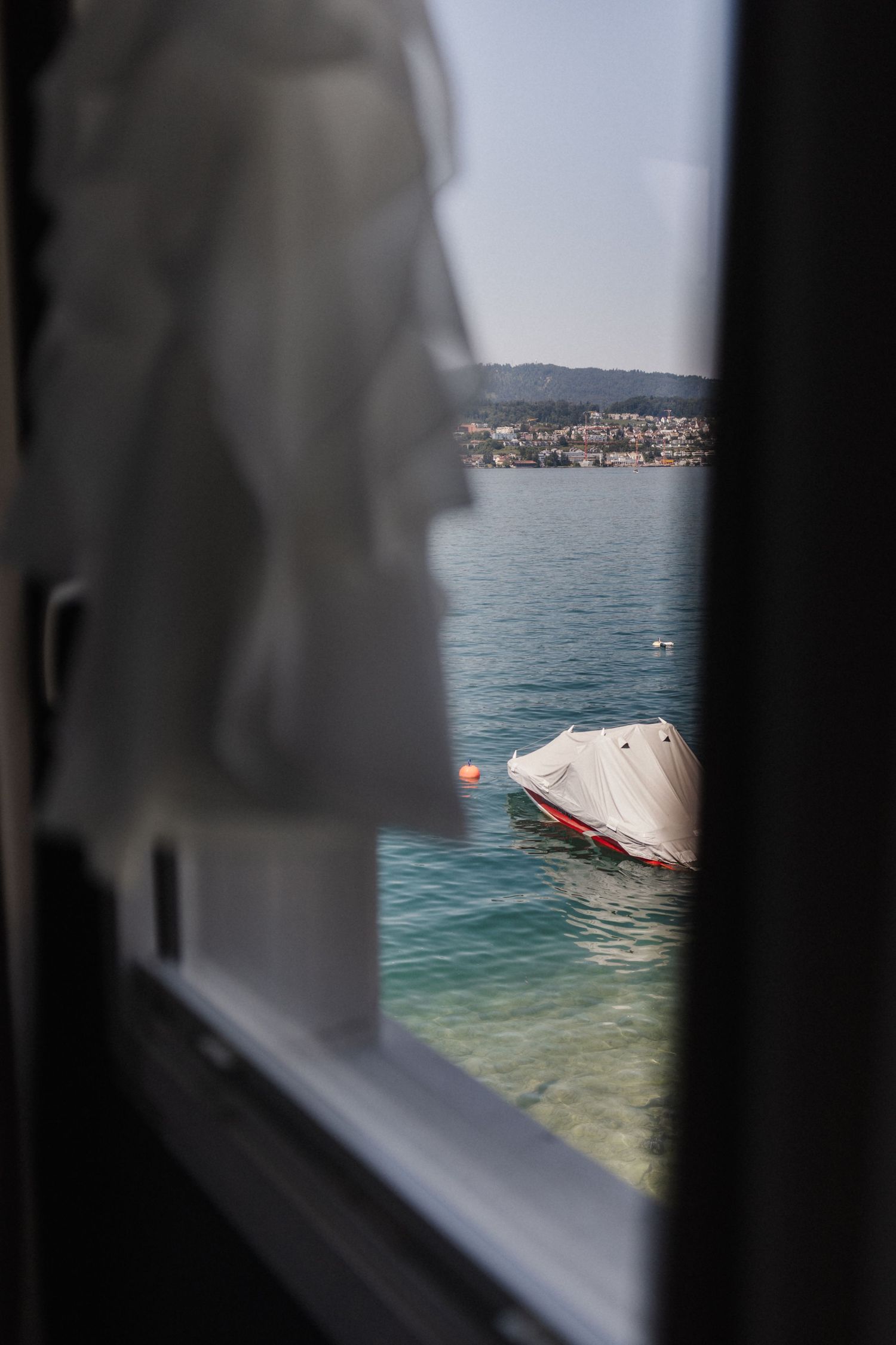View through window of covered boat on turquoise lake with hillside town.
