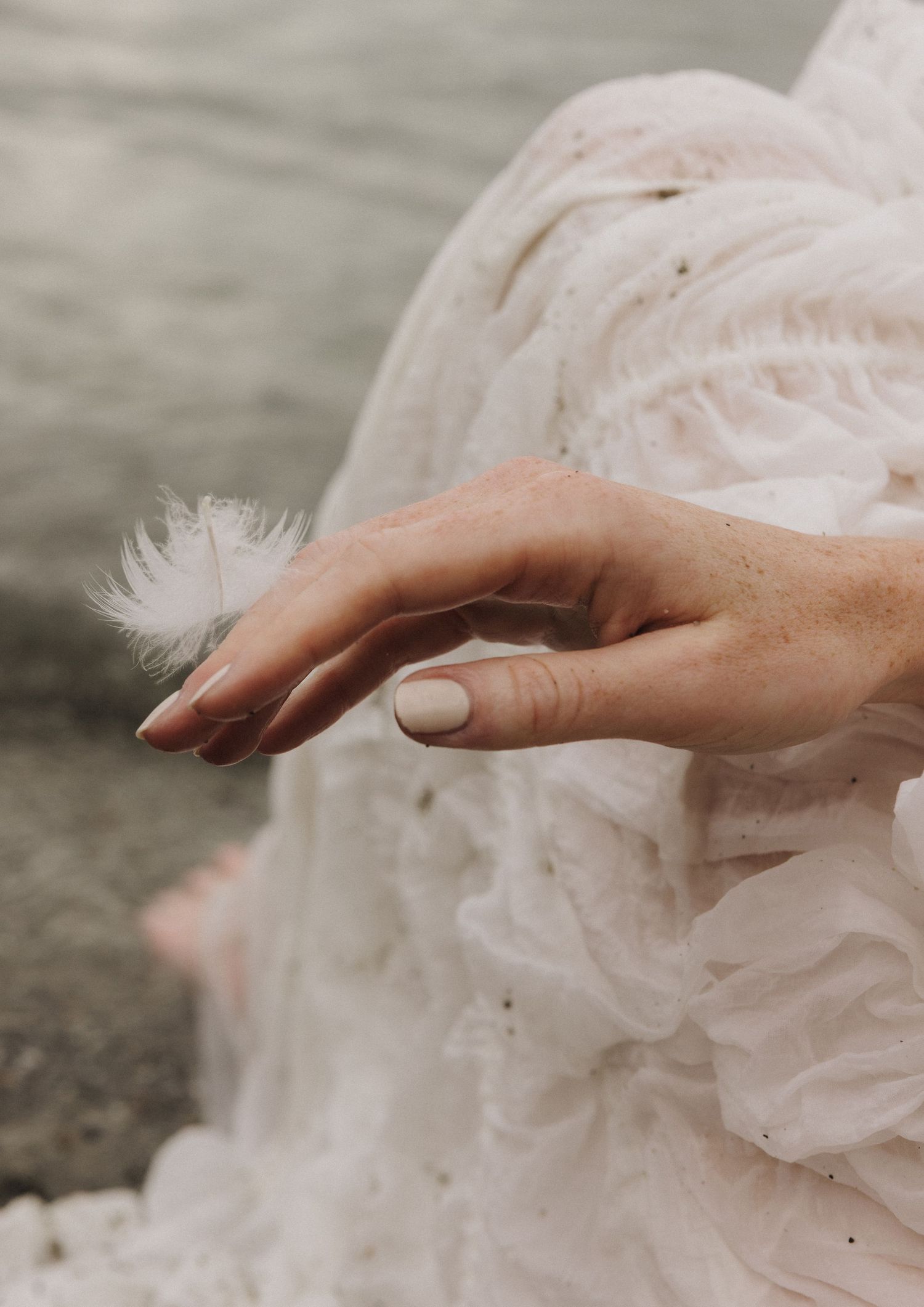 Close-up of a woman in white tulle dress delicately holding a small white feather.