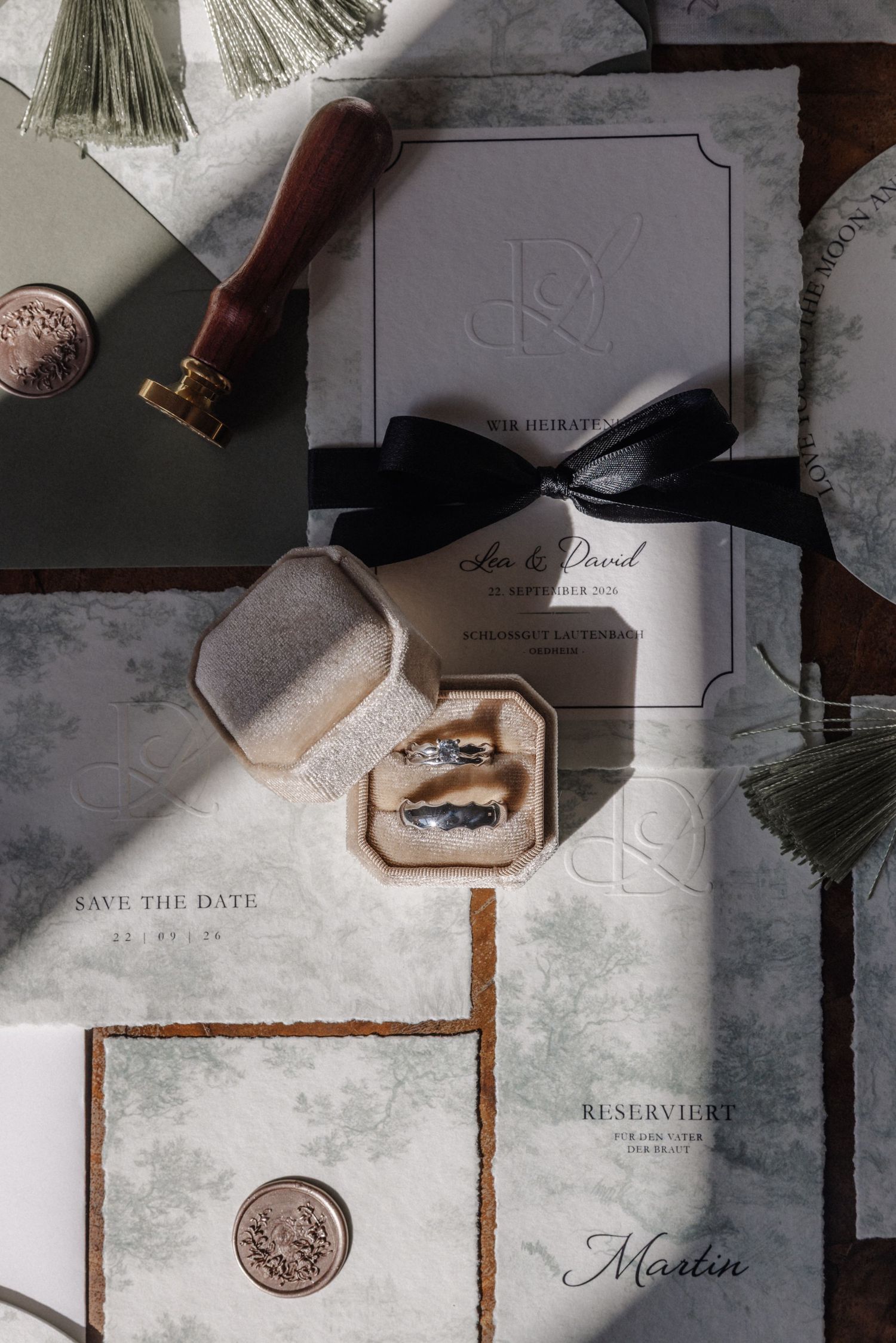Elegant wedding stationery flatlay with rings, wax seal, black ribbon, and marble-textured invitation suite.