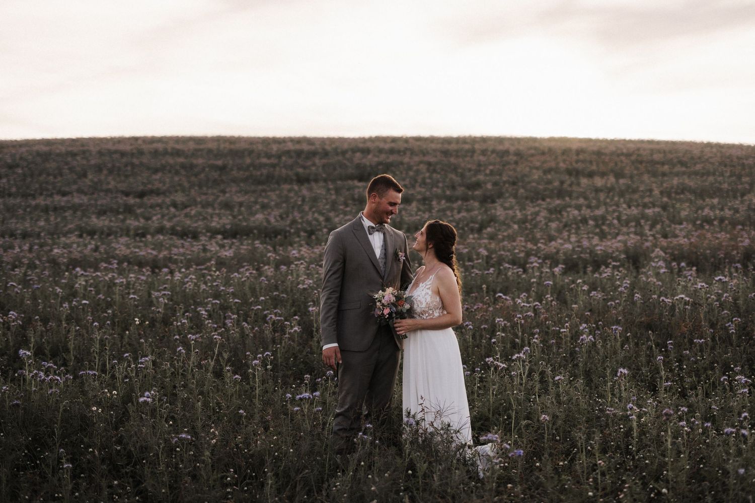 Bride and groom share a tender moment standing together in a blooming field at golden hour.
