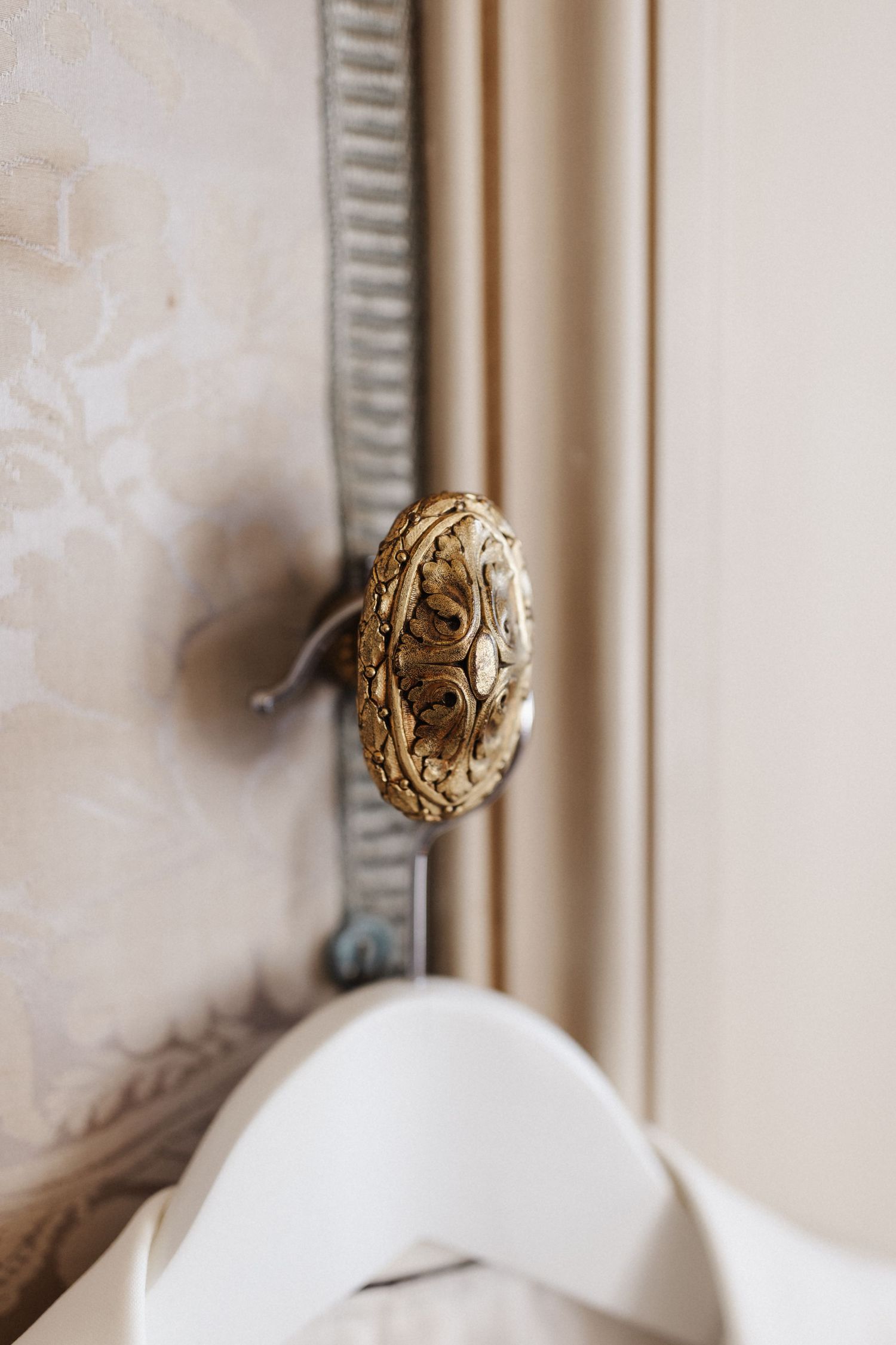 Ornate gold decorative door knob with intricate floral detail against beige damask wallpaper.