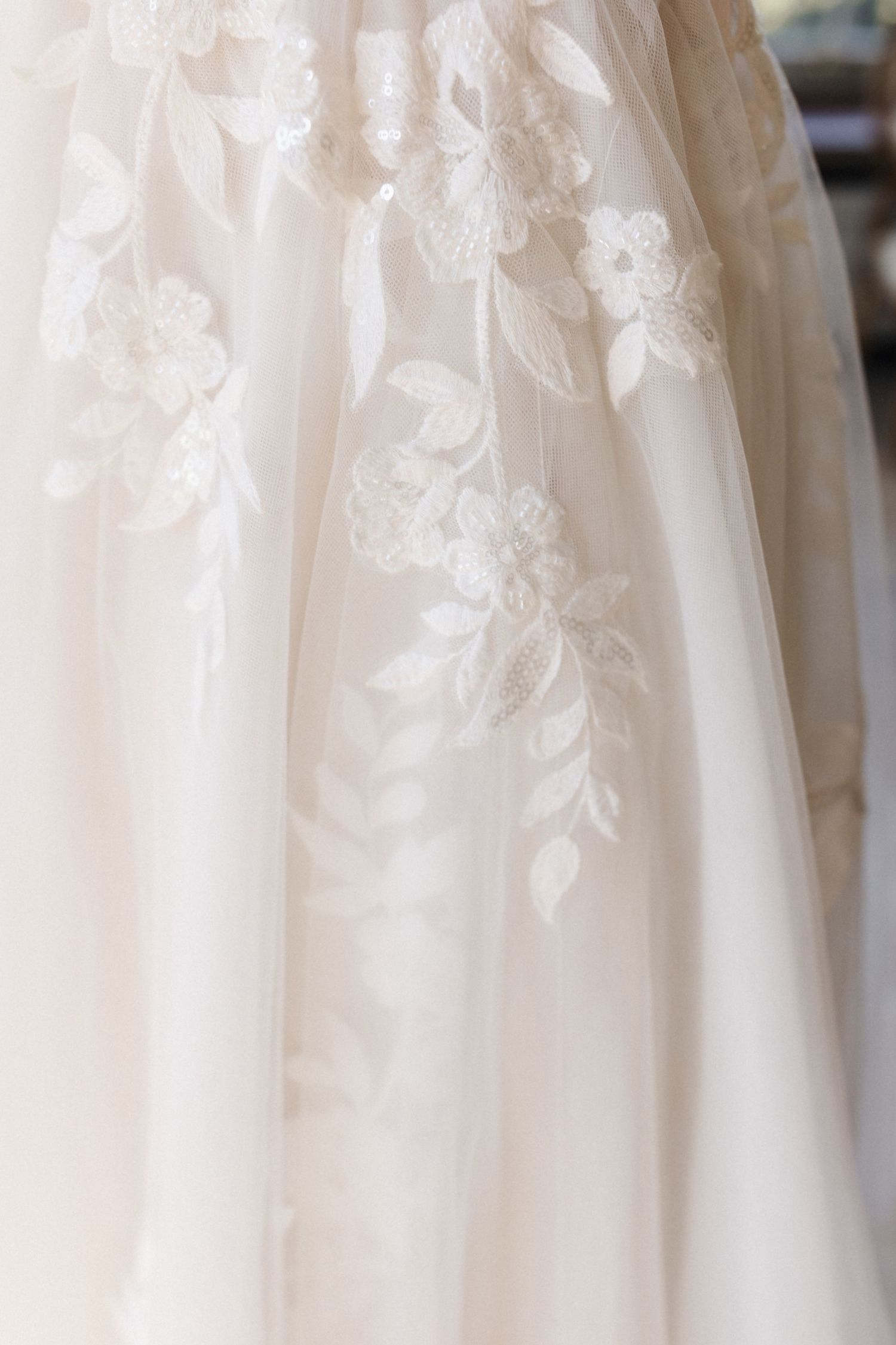 Close-up of a white wedding dress featuring delicate floral lace embroidery on soft tulle fabric.