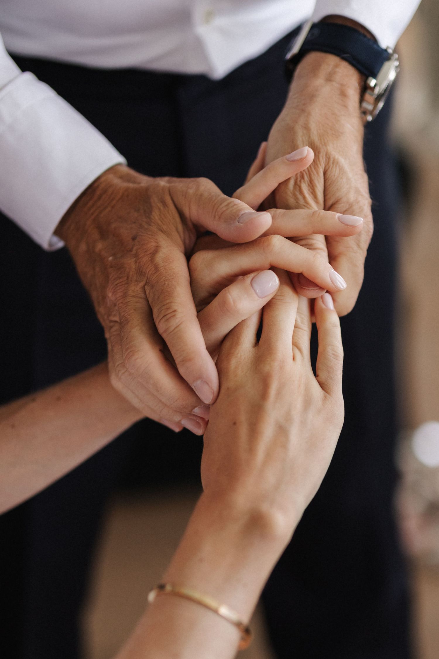 Close-up of older hands gently holding young woman's hands with bracelet.