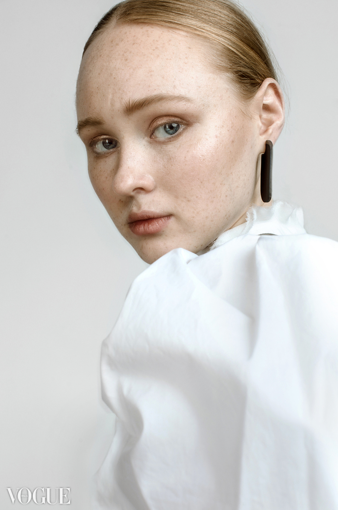 Close-up portrait of a freckled young woman with blue eyes wearing a white shirt and dark drop earring.