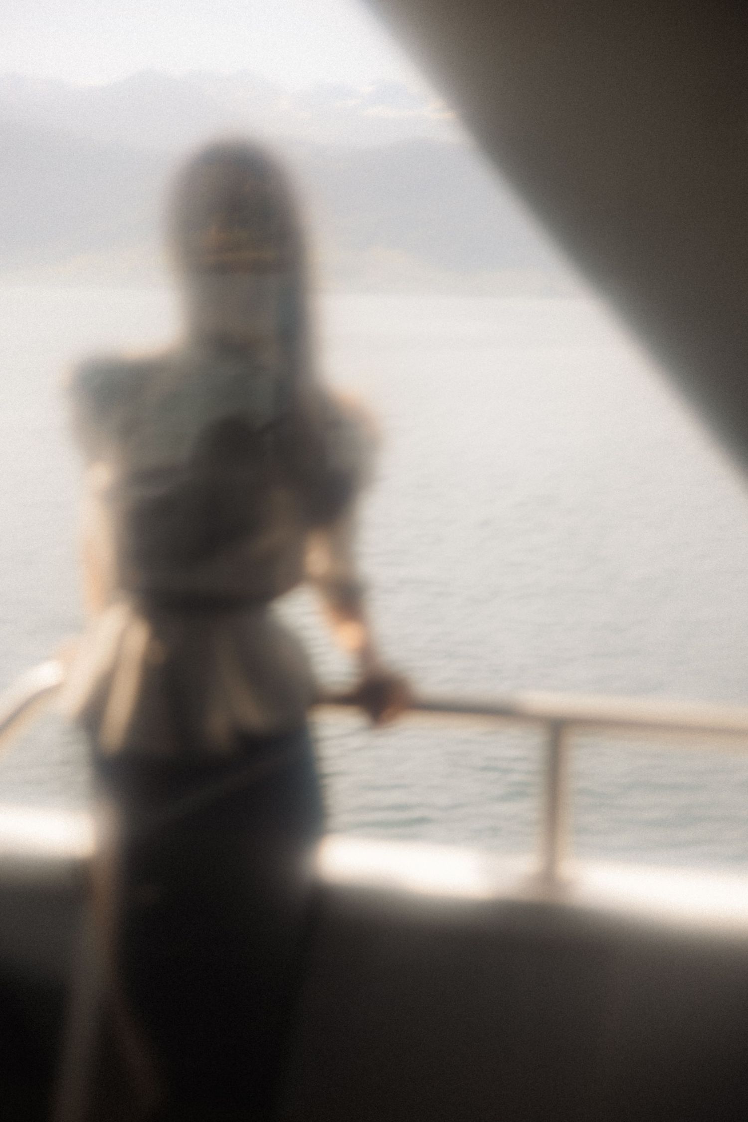 Artistic blurred silhouette of model on boat deck overlooking serene water for Harper's Bazaar fashion editorial.