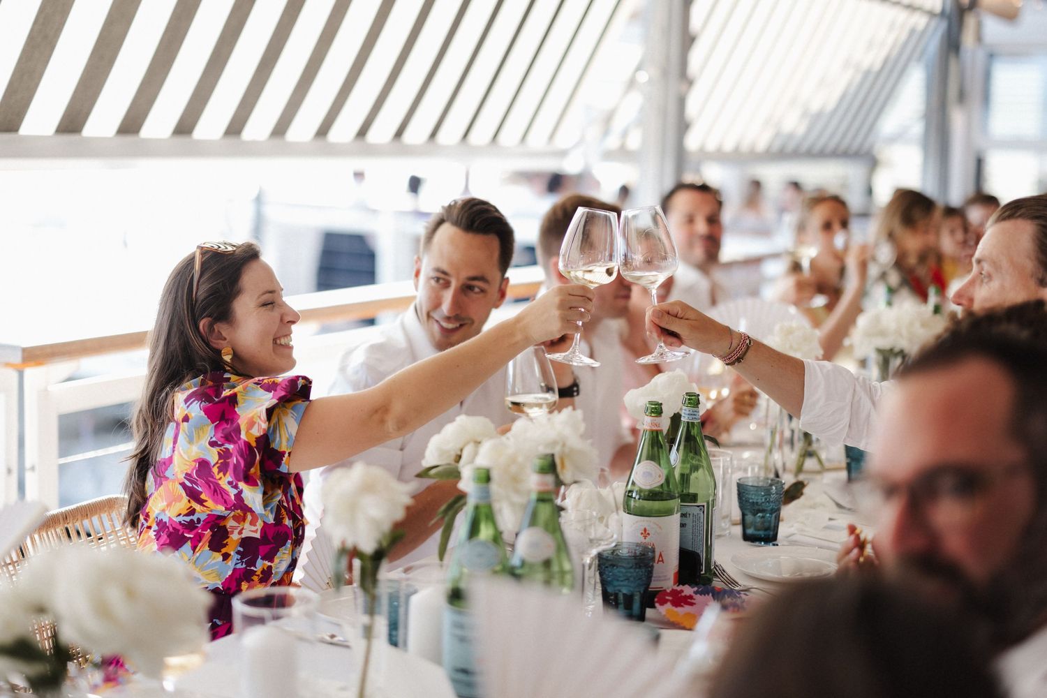 Wedding guests raising glasses in a toast at a beautifully decorated waterfront dining table.