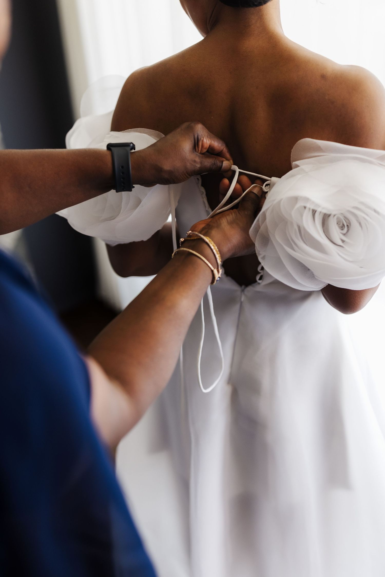 Close-up of hands tying ribbon on back of white ruffled organza wedding gown on bride.