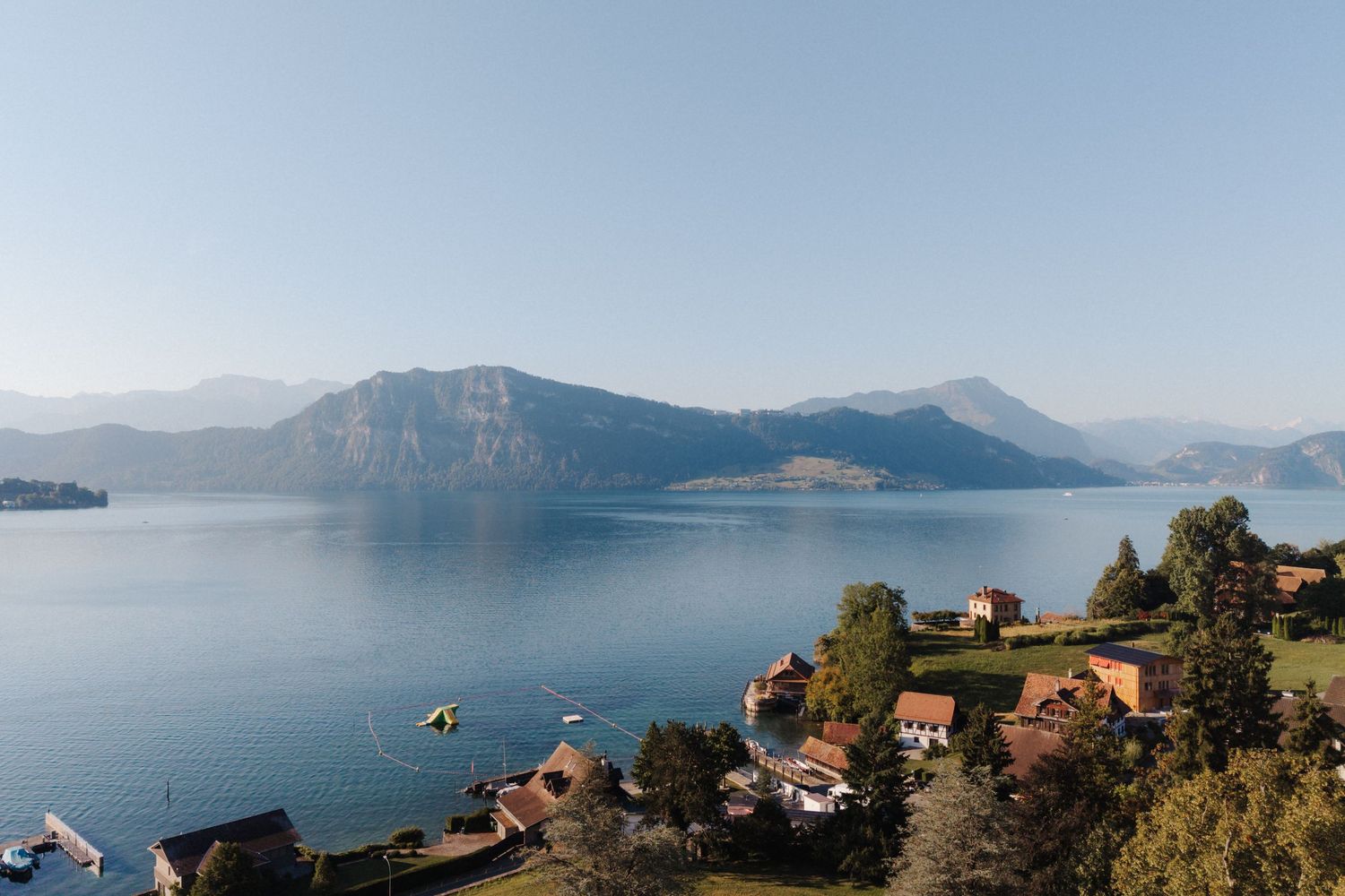 Panoramic view of a picturesque mountain lake with alpine peaks, waterfront village, and clear blue sky.