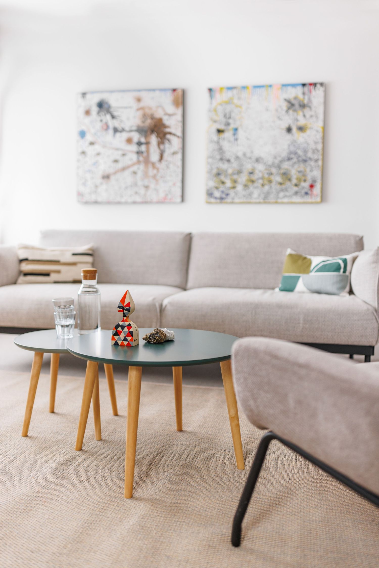 Modern Scandinavian living room with gray sofa, round coffee tables, and abstract wall art.