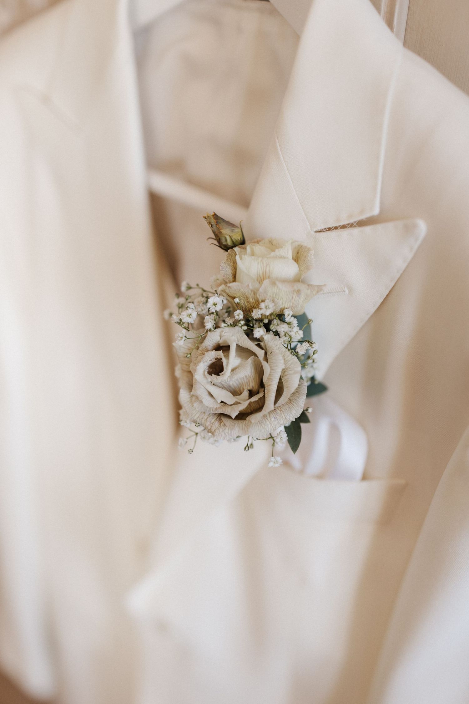 Close-up of white rose and baby's breath boutonniere in pocket of ivory wedding suit jacket.