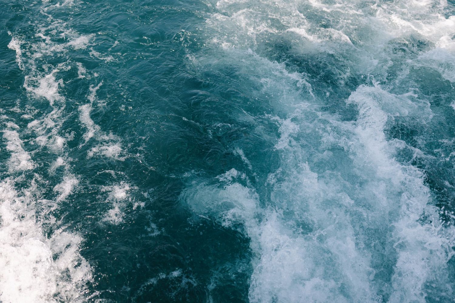 Aerial view of deep blue ocean water with white foamy wake trailing behind a moving boat.