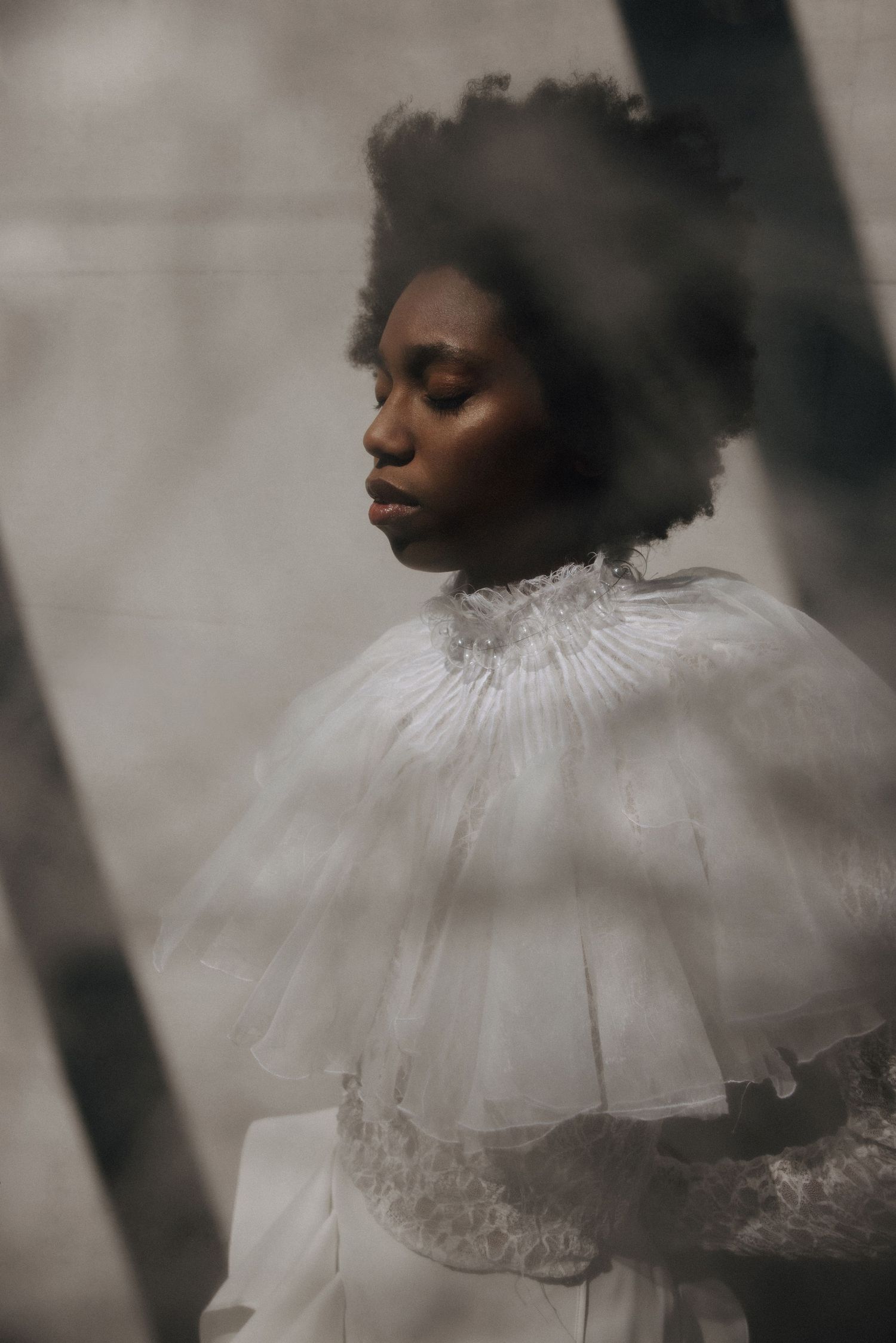 Dreamy fashion portrait of model in white ruffled cape dress shot through glass with blur.