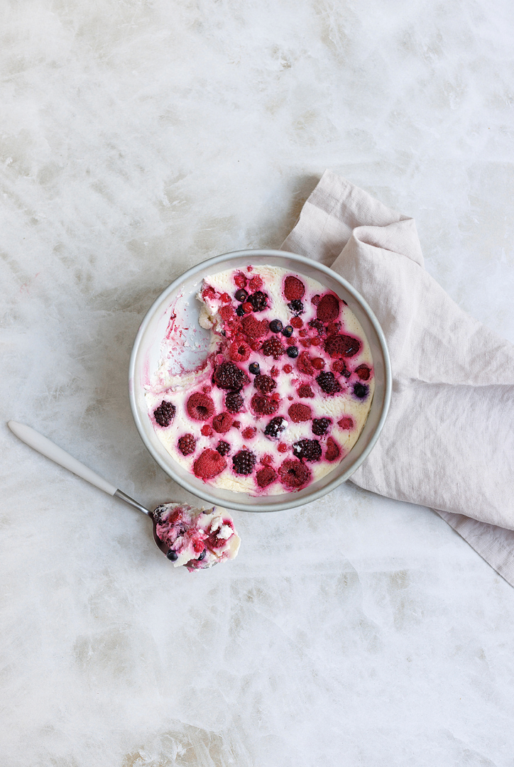 Overhead view of a creamy berry bowl with raspberries and blackberries on a marble surface.