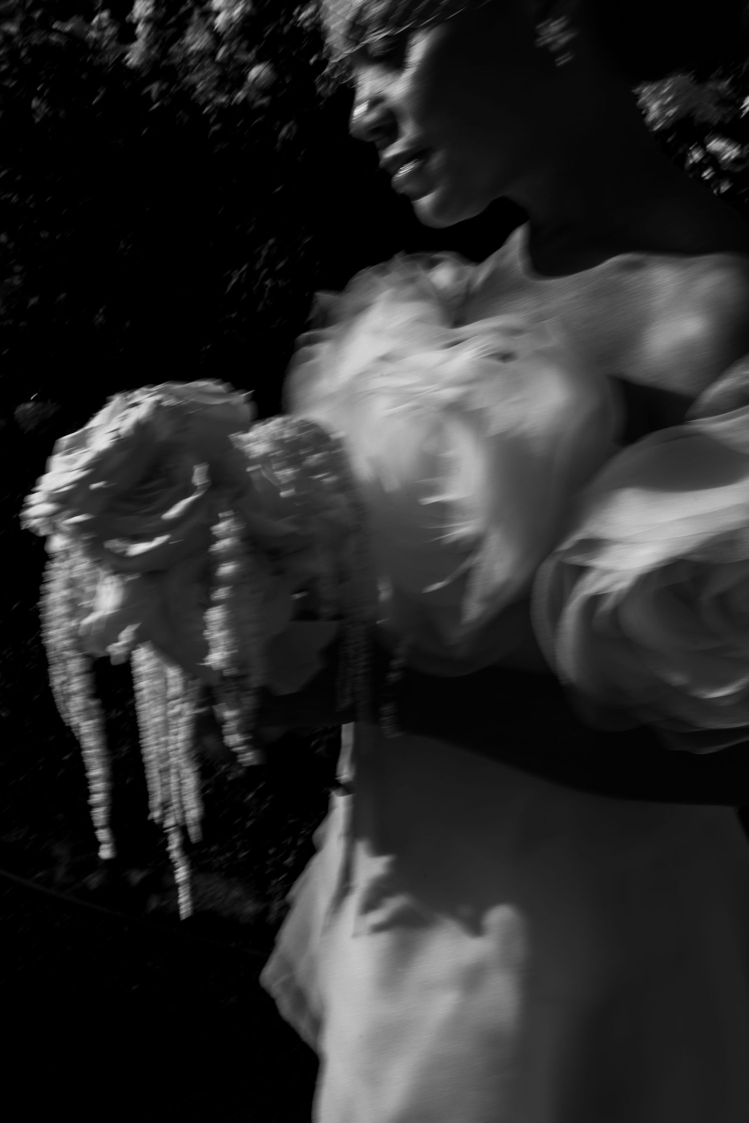Black and white artistic photo of bride in white dress holding bouquet with dramatic lighting.
