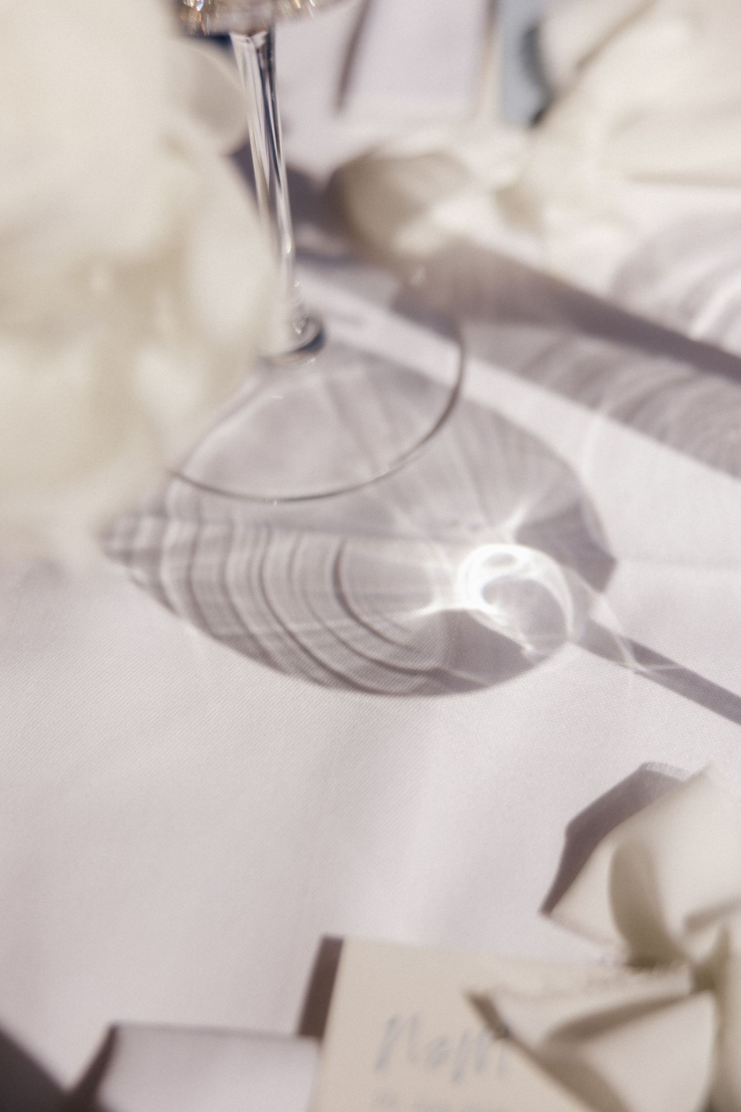 Artistic shadow of a wine glass stem casting geometric patterns on a white wedding table linen.