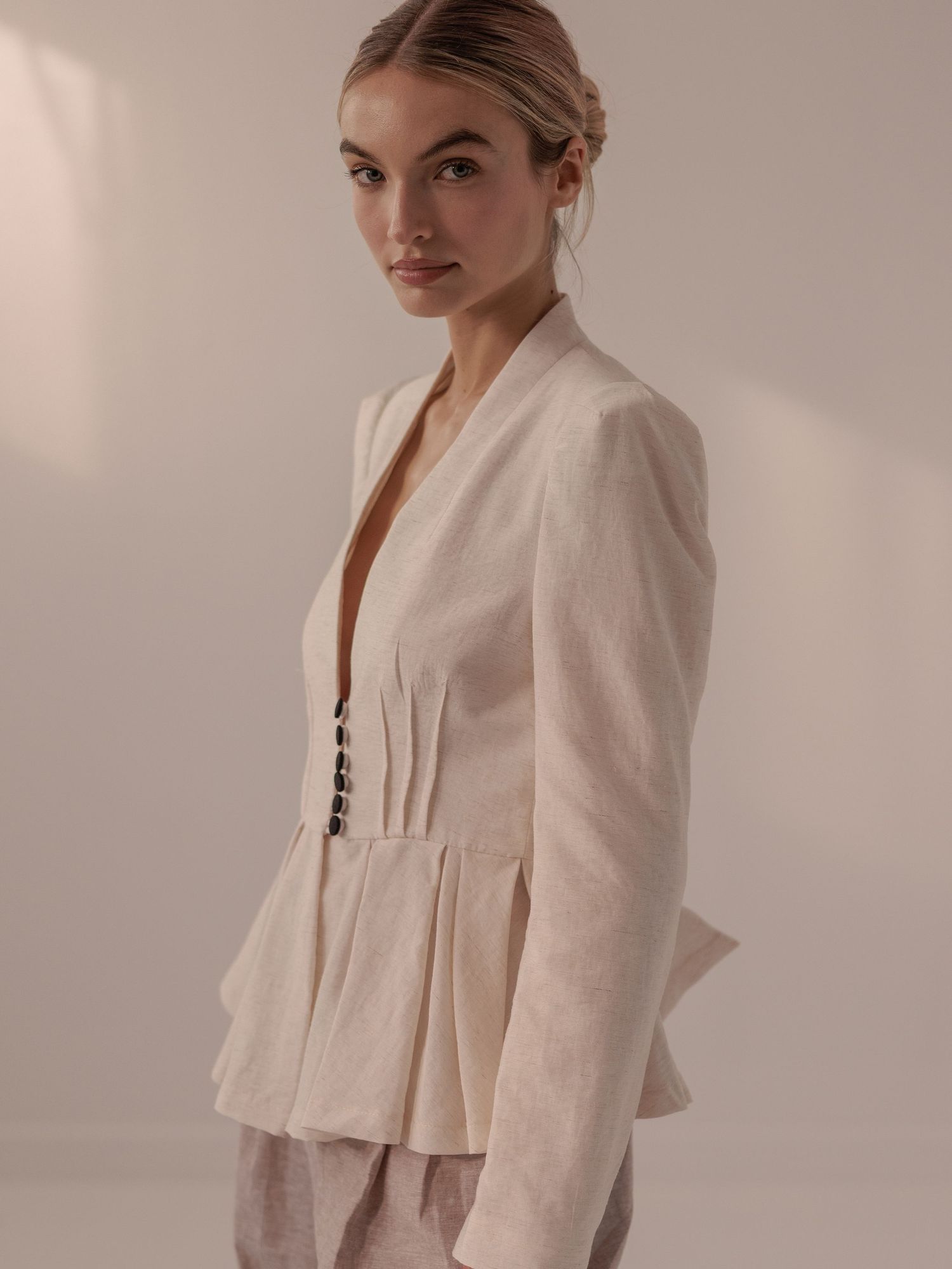 Model wearing a structured cream linen peplum blazer with button detail and wide-leg trousers.