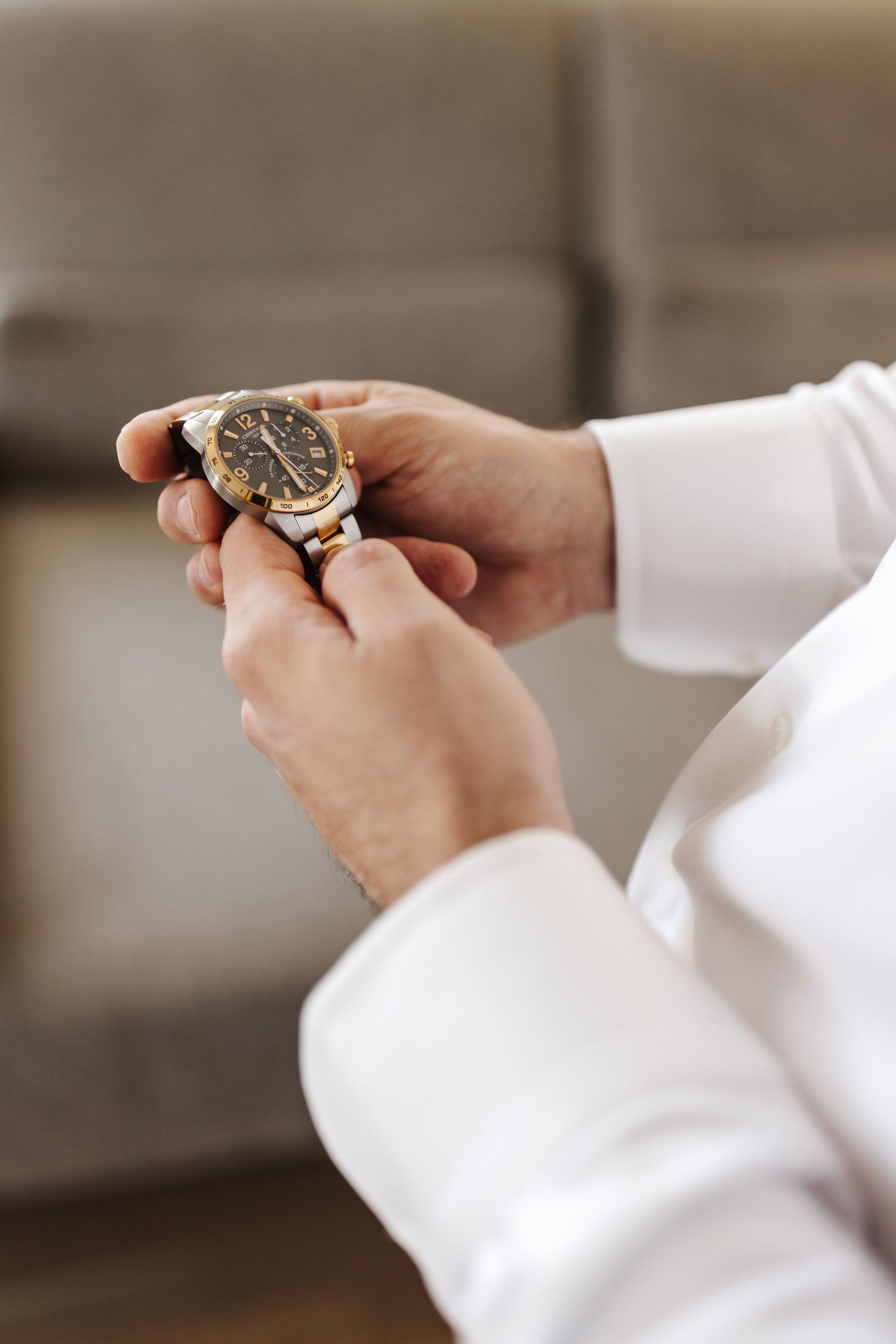 Groom in white shirt fastening a two-tone gold and silver luxury watch on his wrist.