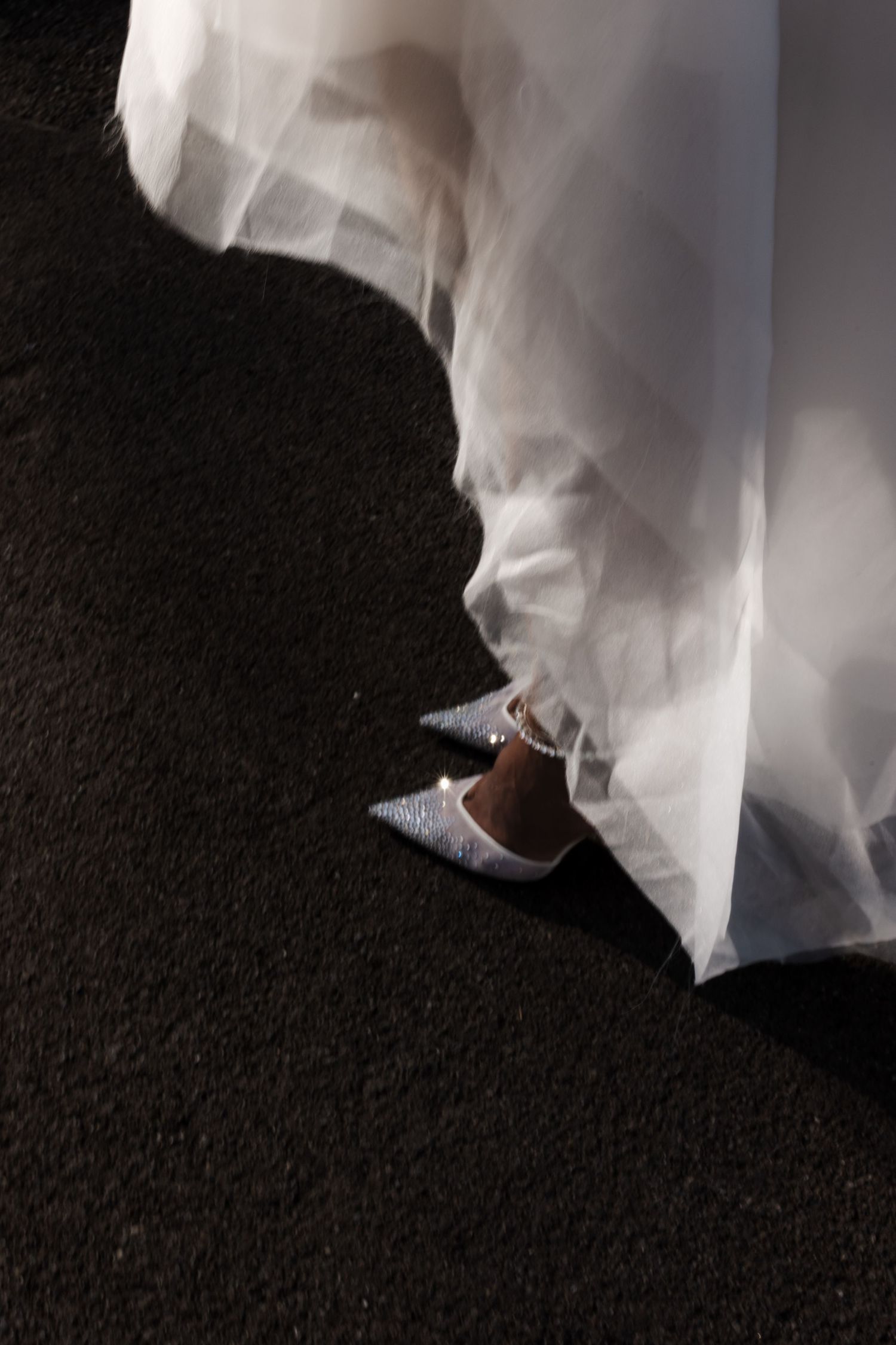 Close-up of bride's sparkling heels beneath flowing white tulle wedding dress on pavement.