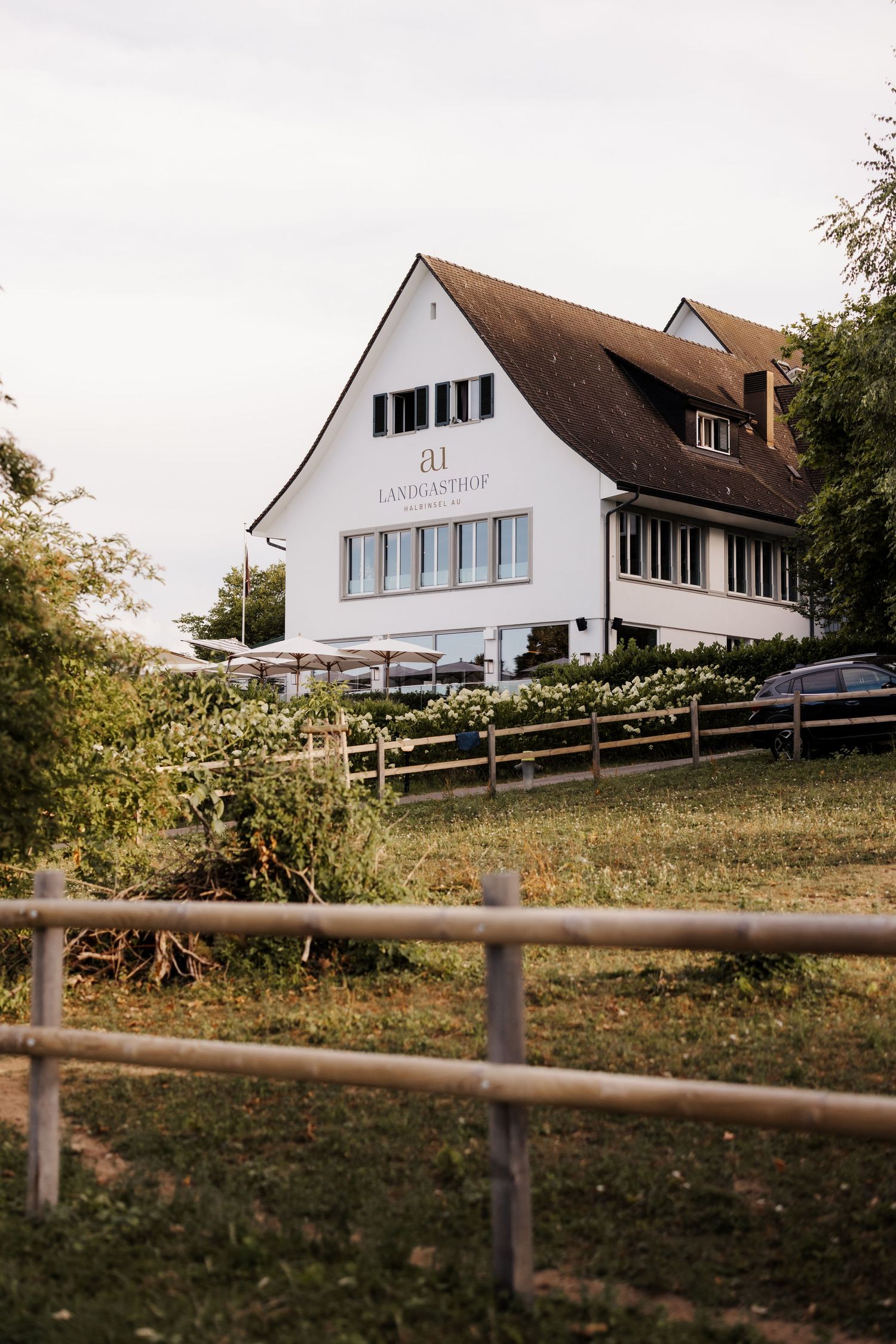 White country inn building with brown roof, wooden fence, and green surroundings at dusk.