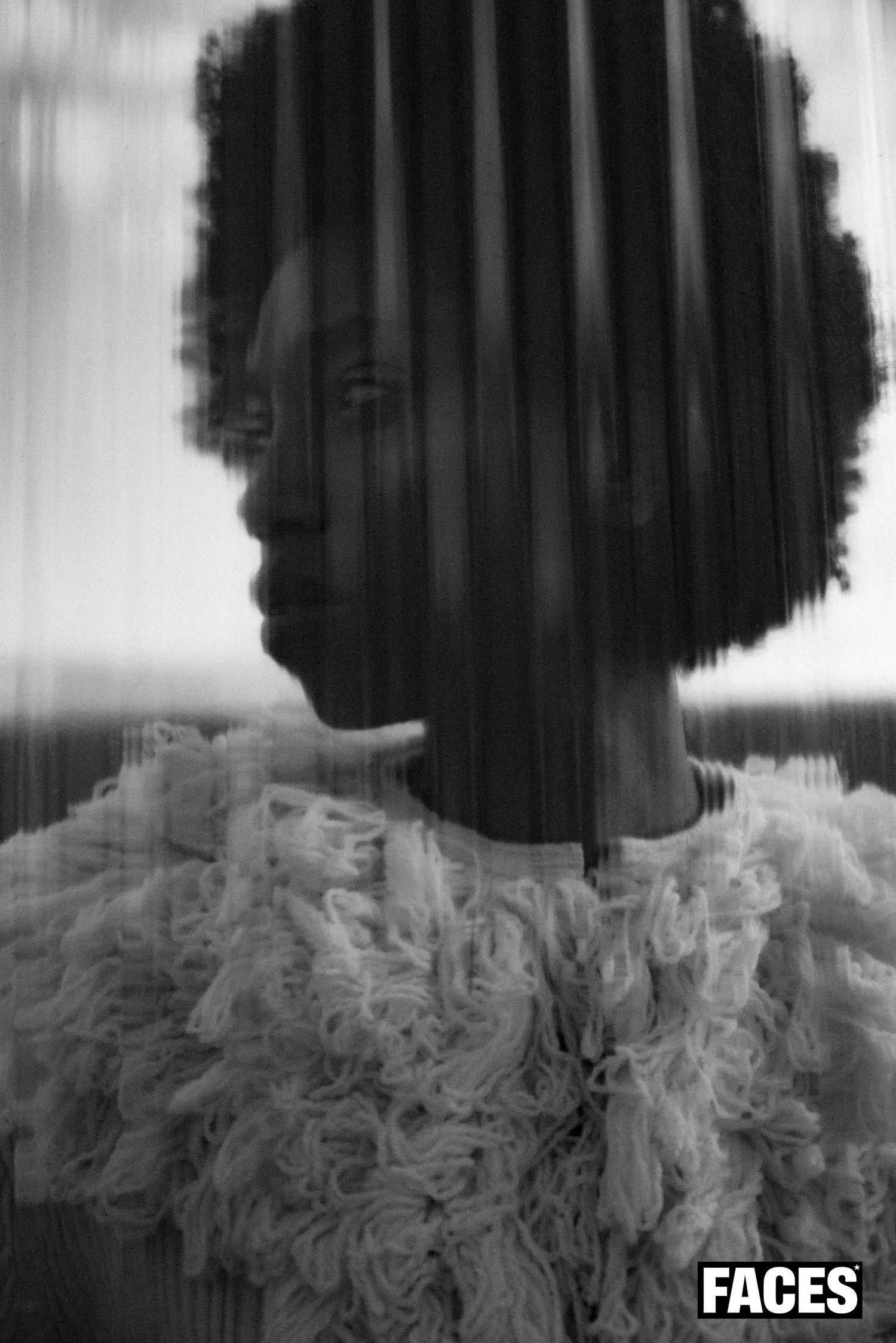 Black and white portrait of a model in a ruffled white top, shot through vertical lines creating a striped effect.