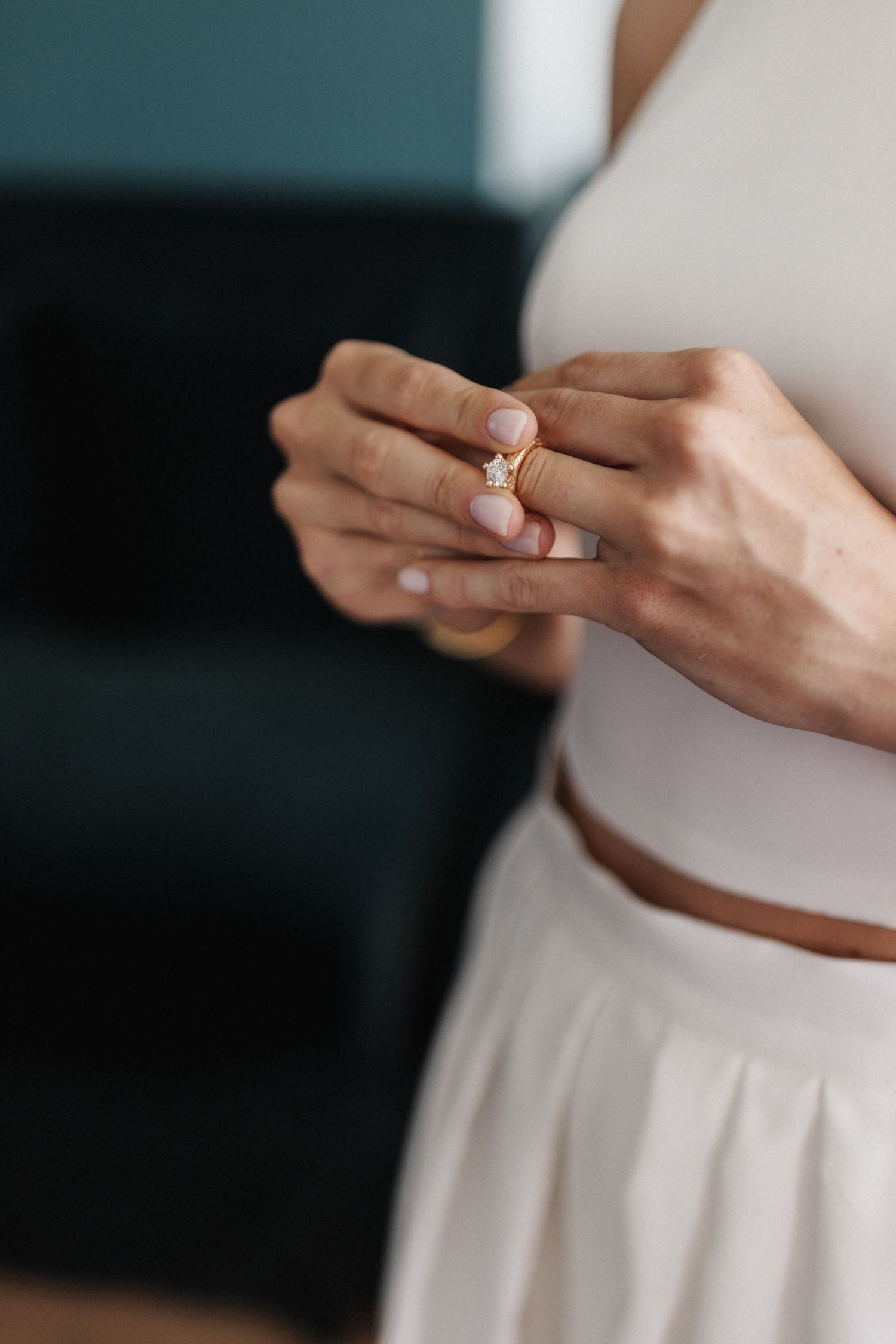 Close-up of a bride's hands holding a gold diamond engagement ring against her white wedding dress.