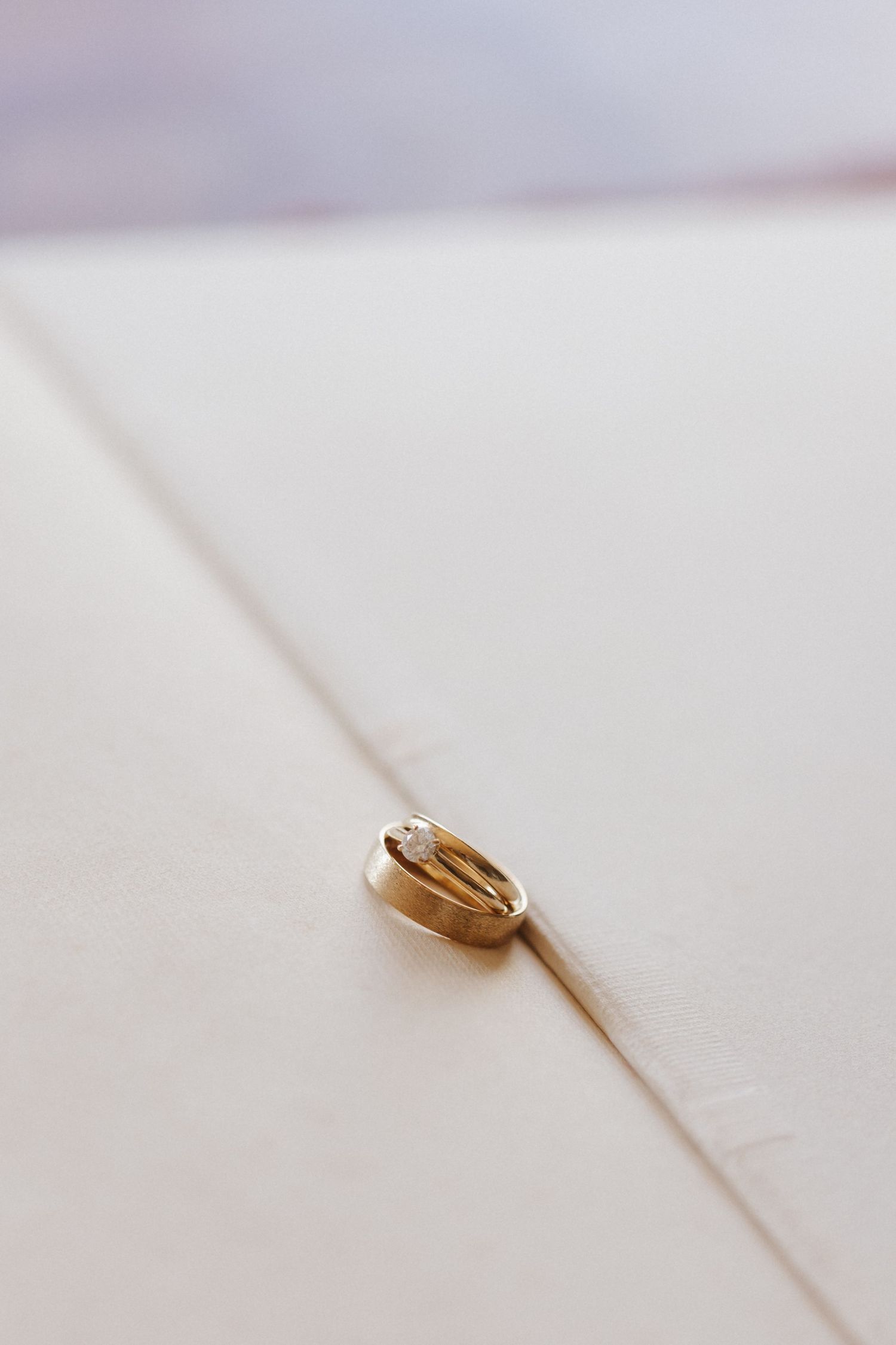Gold wedding bands interlinked on cream textured envelope with soft bokeh background.