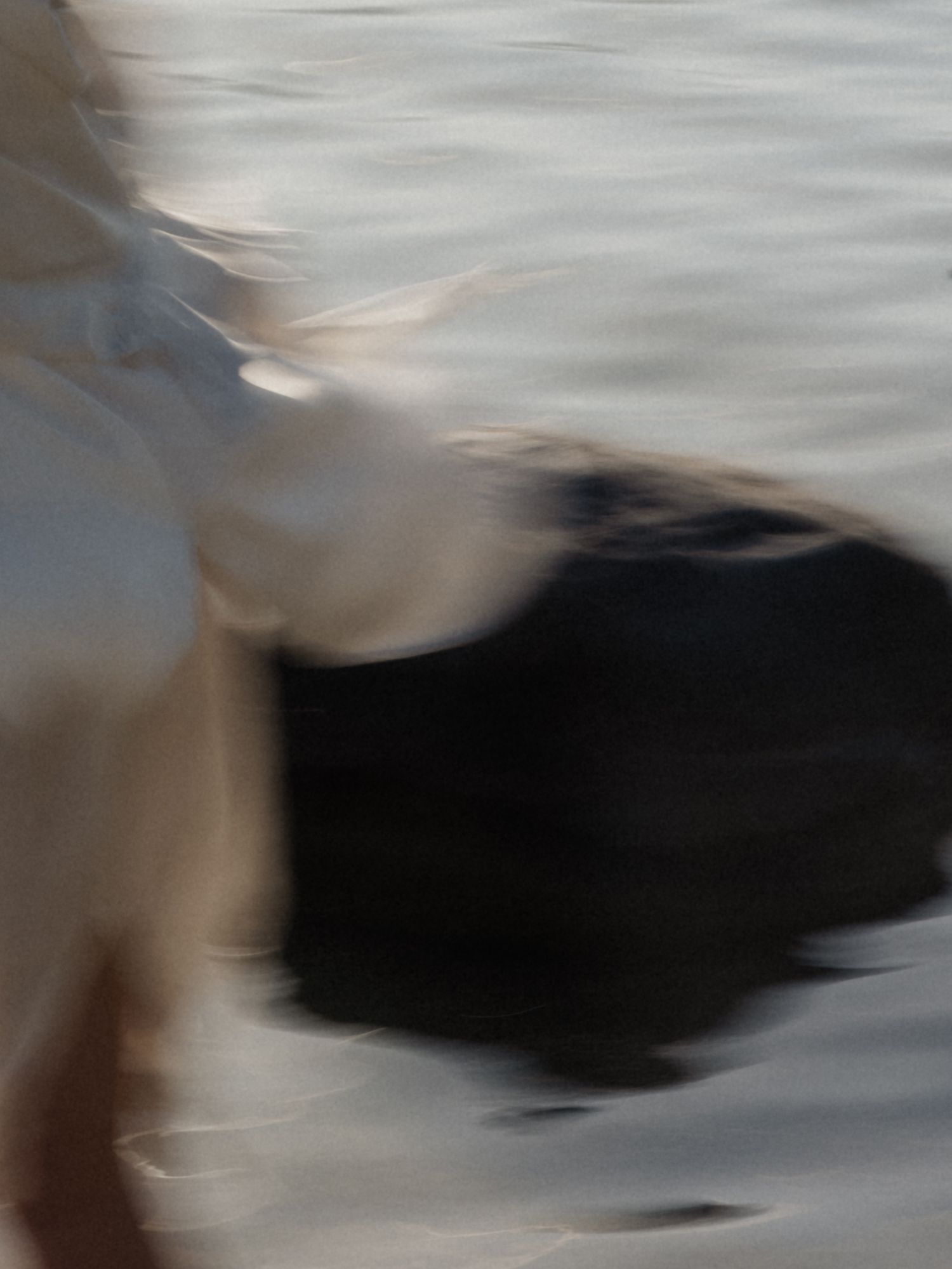 Abstract blurred motion shot of white fabric and black swimsuit near rippling water.