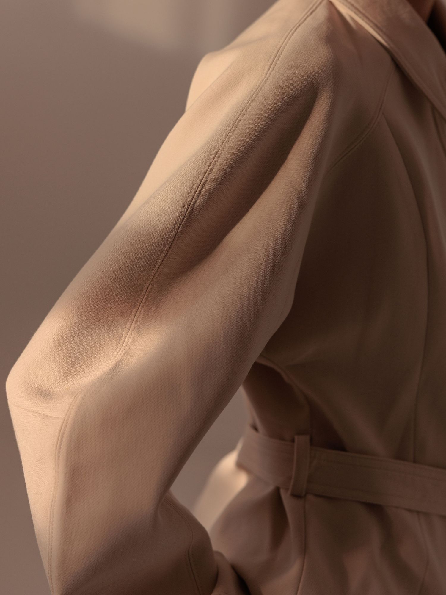 Close-up of a beige jacket sleeve showing structured seam detail and a belted waist.
