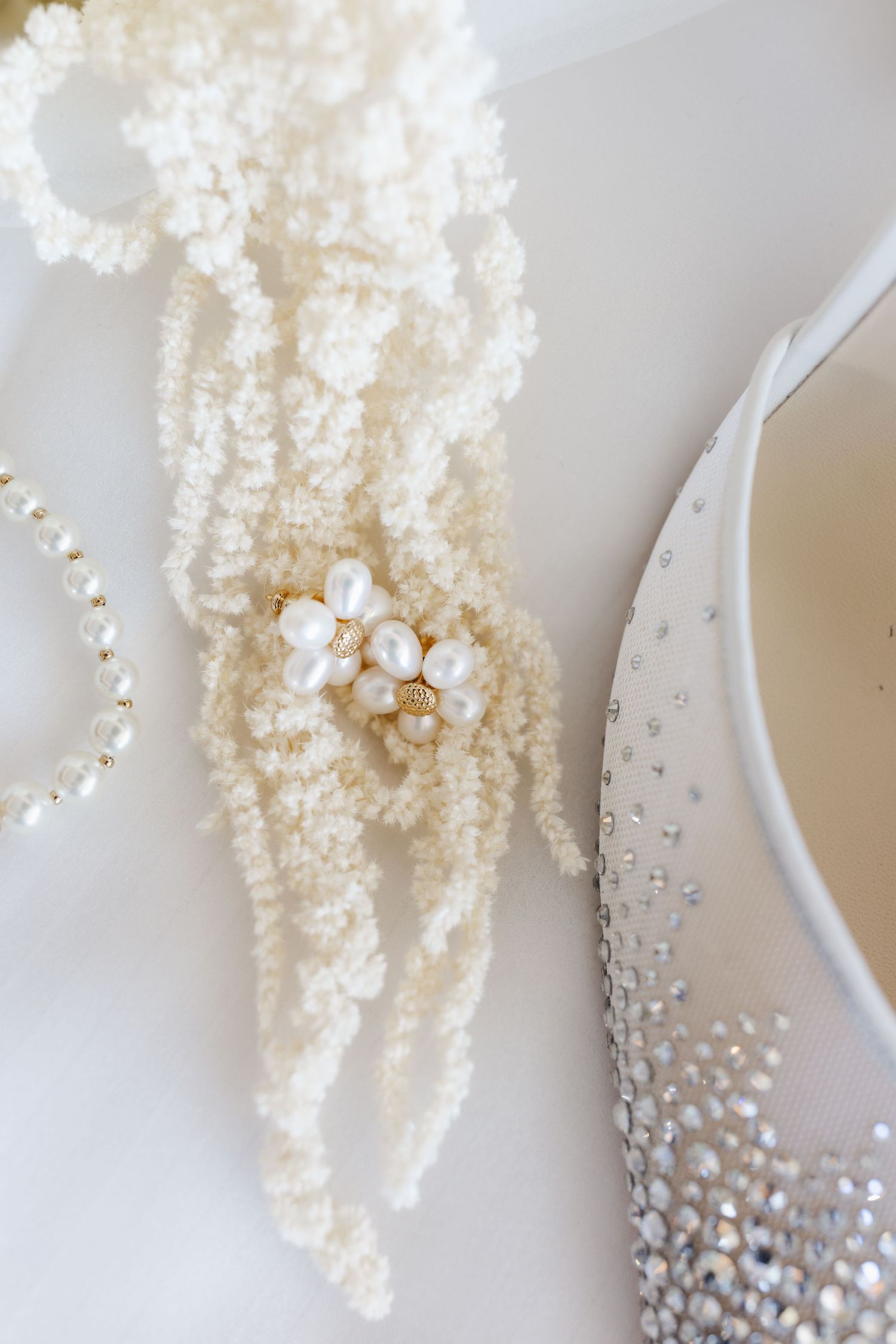 Pearl cluster earrings displayed on twisted ivory seed pearl necklace beside crystal embellished bridal shoe.