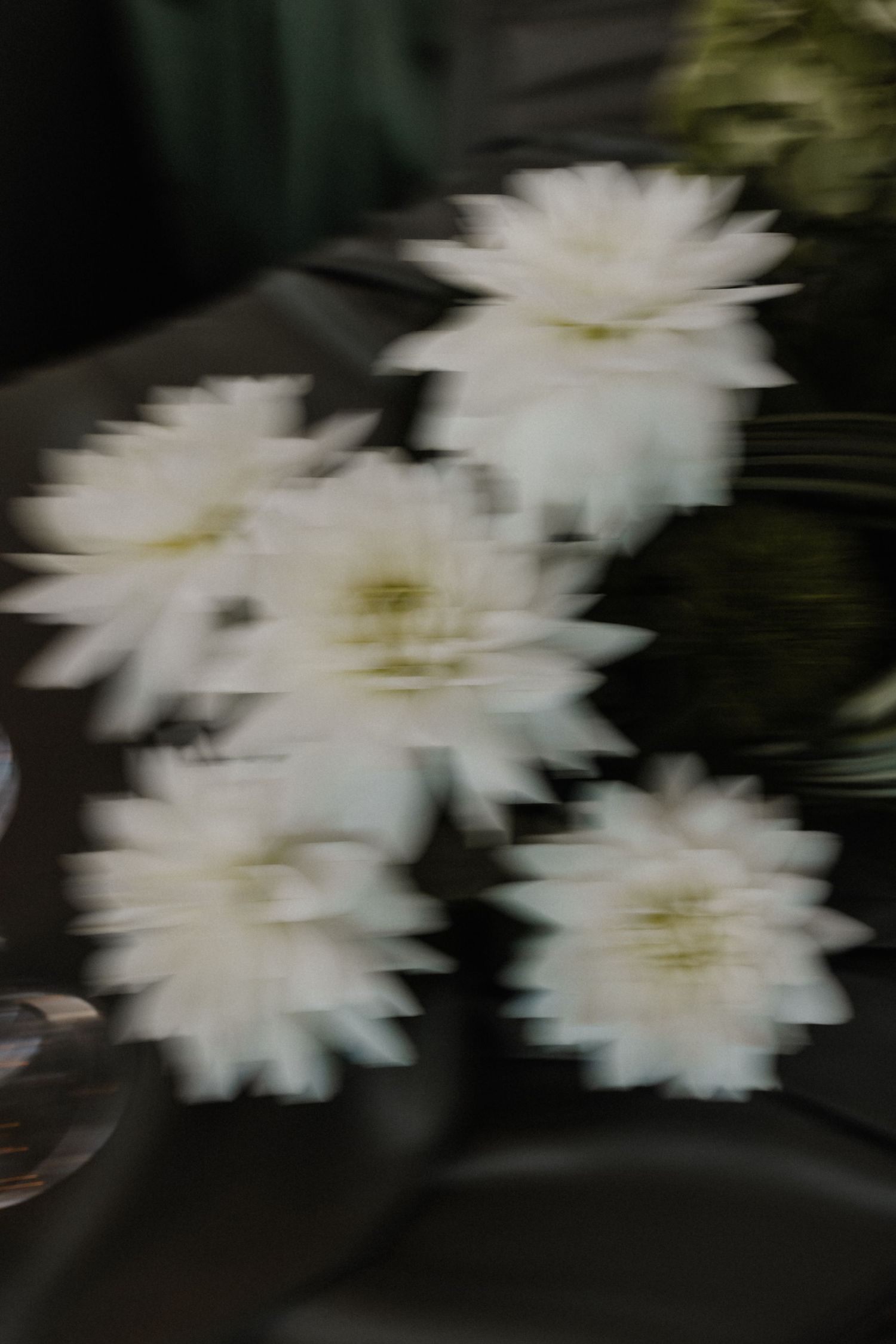 Artistic blurred close-up of white dahlia flowers on dark wedding reception table setting.