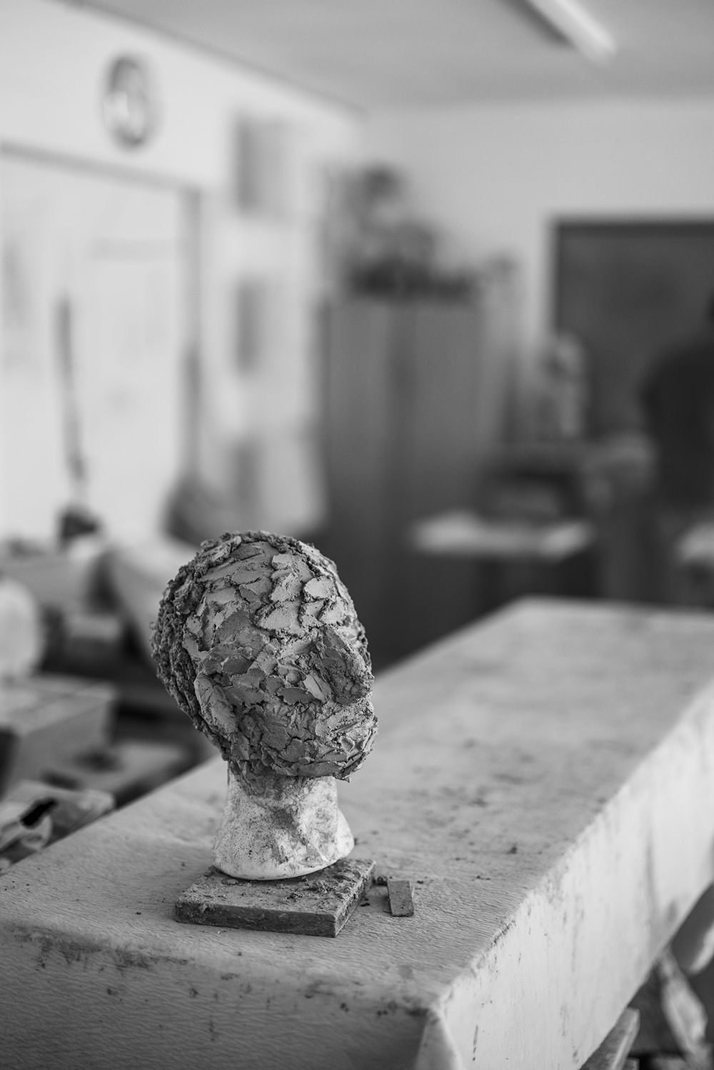 Textured sculptural bust of a human head displayed on a workbench in an artist studio.