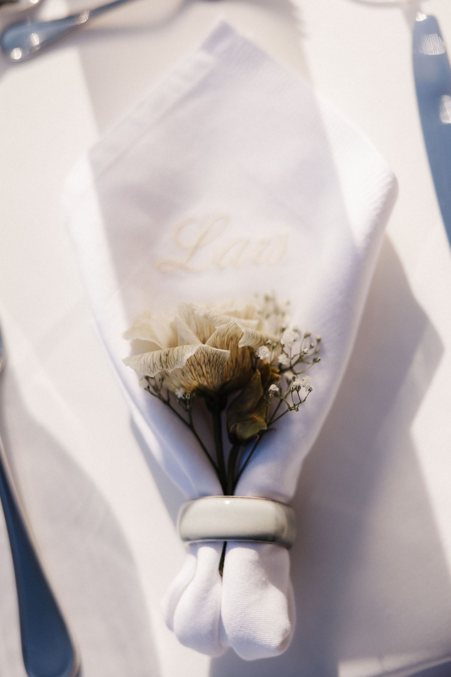 Elegant white wedding napkin with gold monogram and dried floral boutonniere in a silver napkin ring.