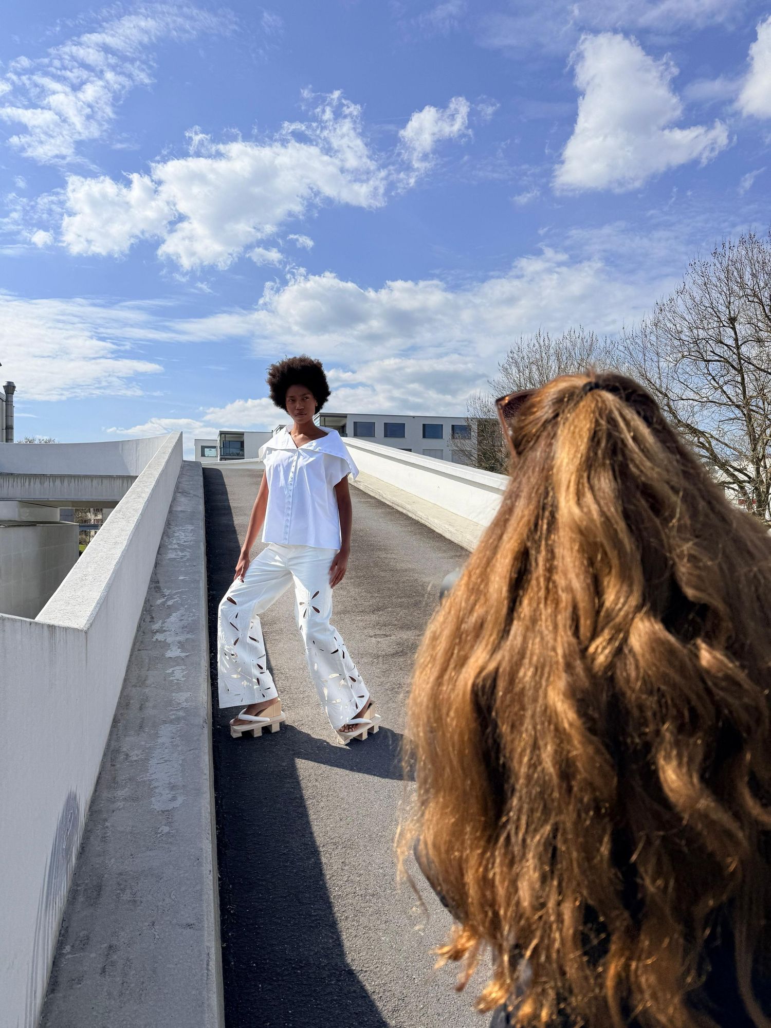 Photographer capturing a model in white outfit skateboarding on a rooftop under blue sky.