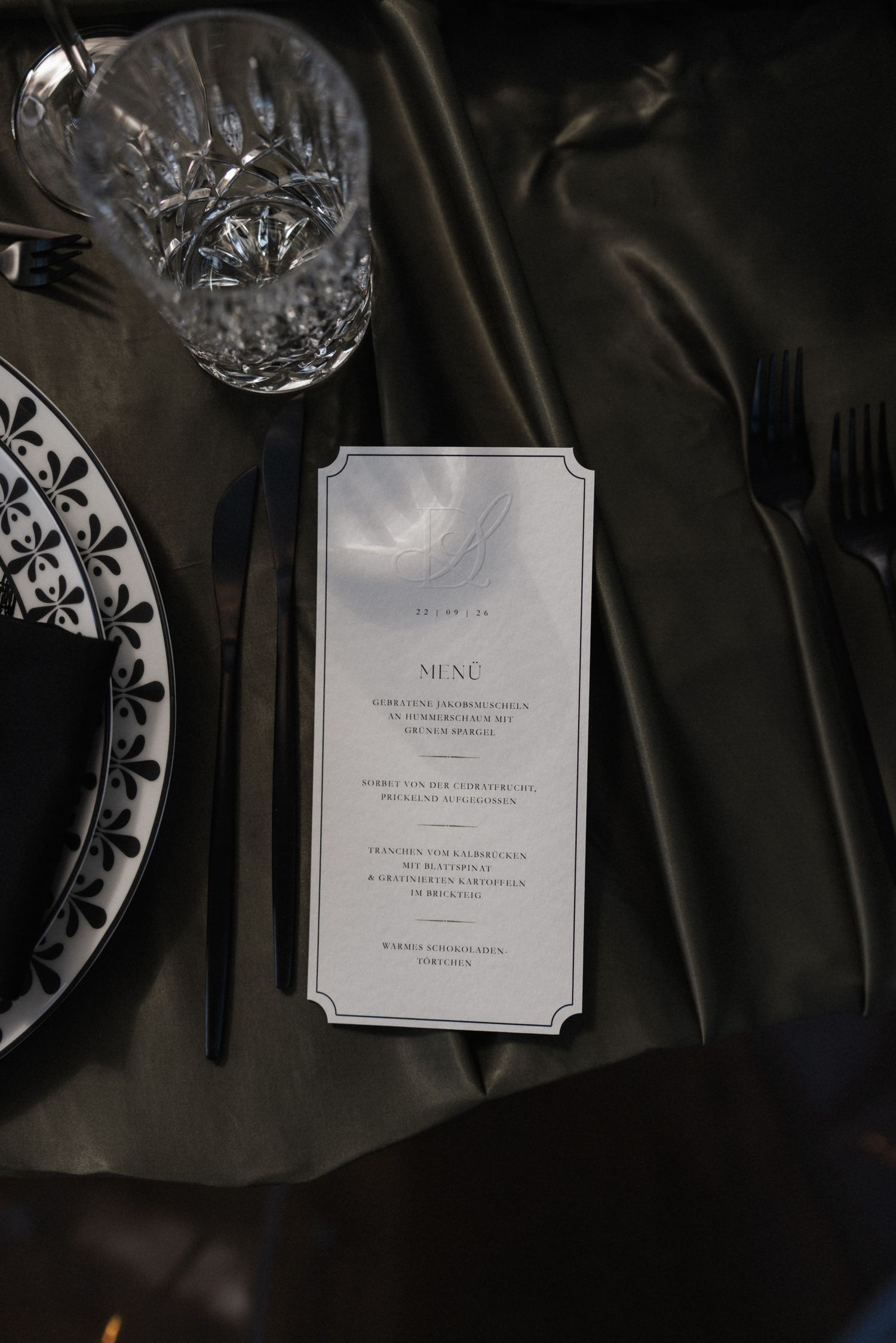 Elegant wedding table setting with black cutlery, crystal glassware, floral plate, and a menu card.