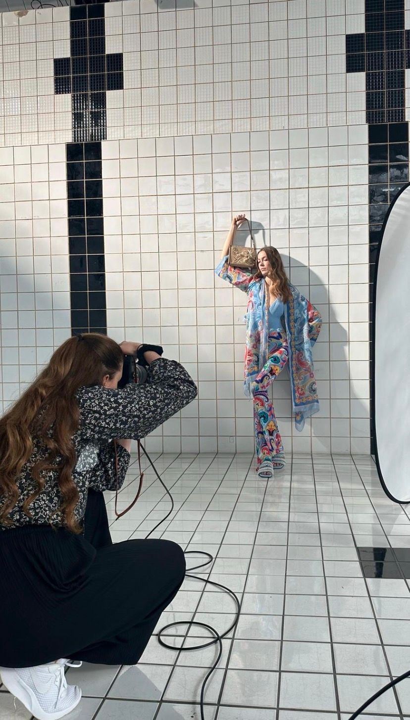 Photographer capturing a model in colorful outfit holding a handbag against tiled wall backdrop.