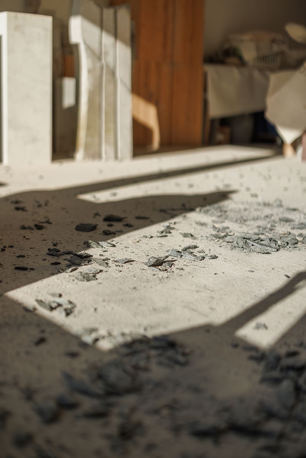 Sunlit dusty workshop floor scattered with stone chips and marble dust fragments.