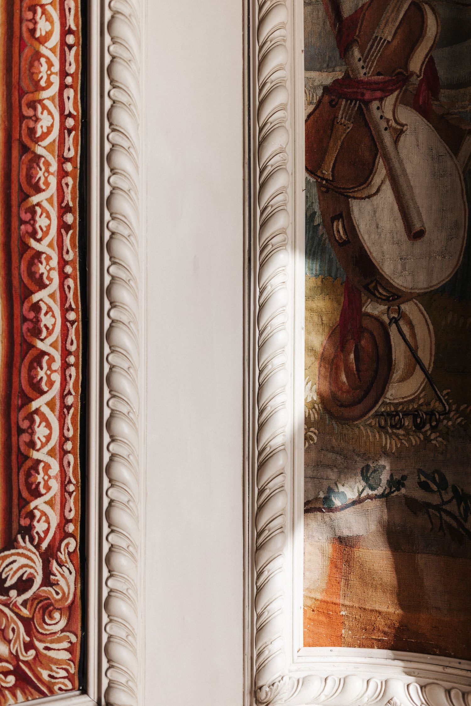 Detail of an ornate white plaster molding beside a classical painting with musical instruments.