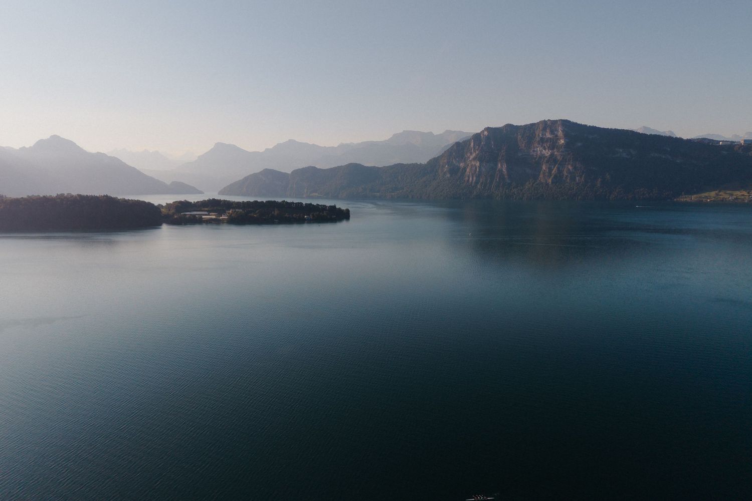 Serene aerial view of a calm mountain lake with misty peaks and a small island in the distance.
