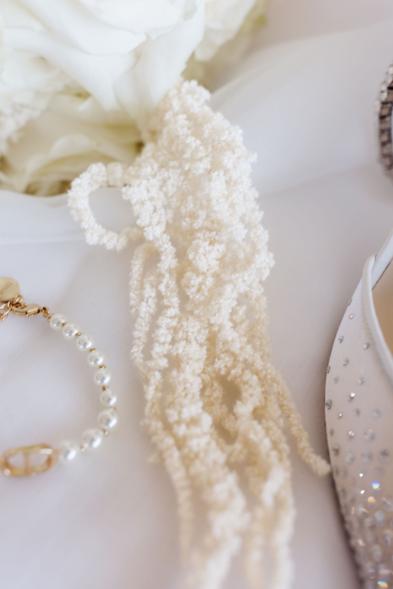 Twisted ivory seed pearl necklace with gold bracelet and crystal bridal heel on white background.