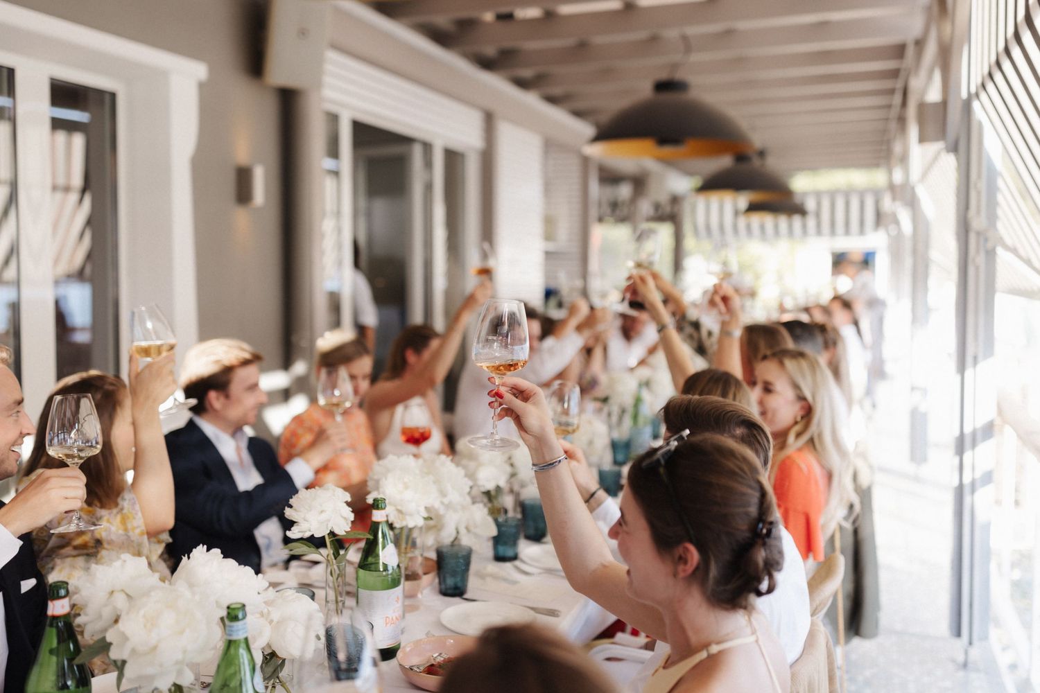 Wedding guests enthusiastically raising glasses in a toast at an elegant outdoor reception dinner.