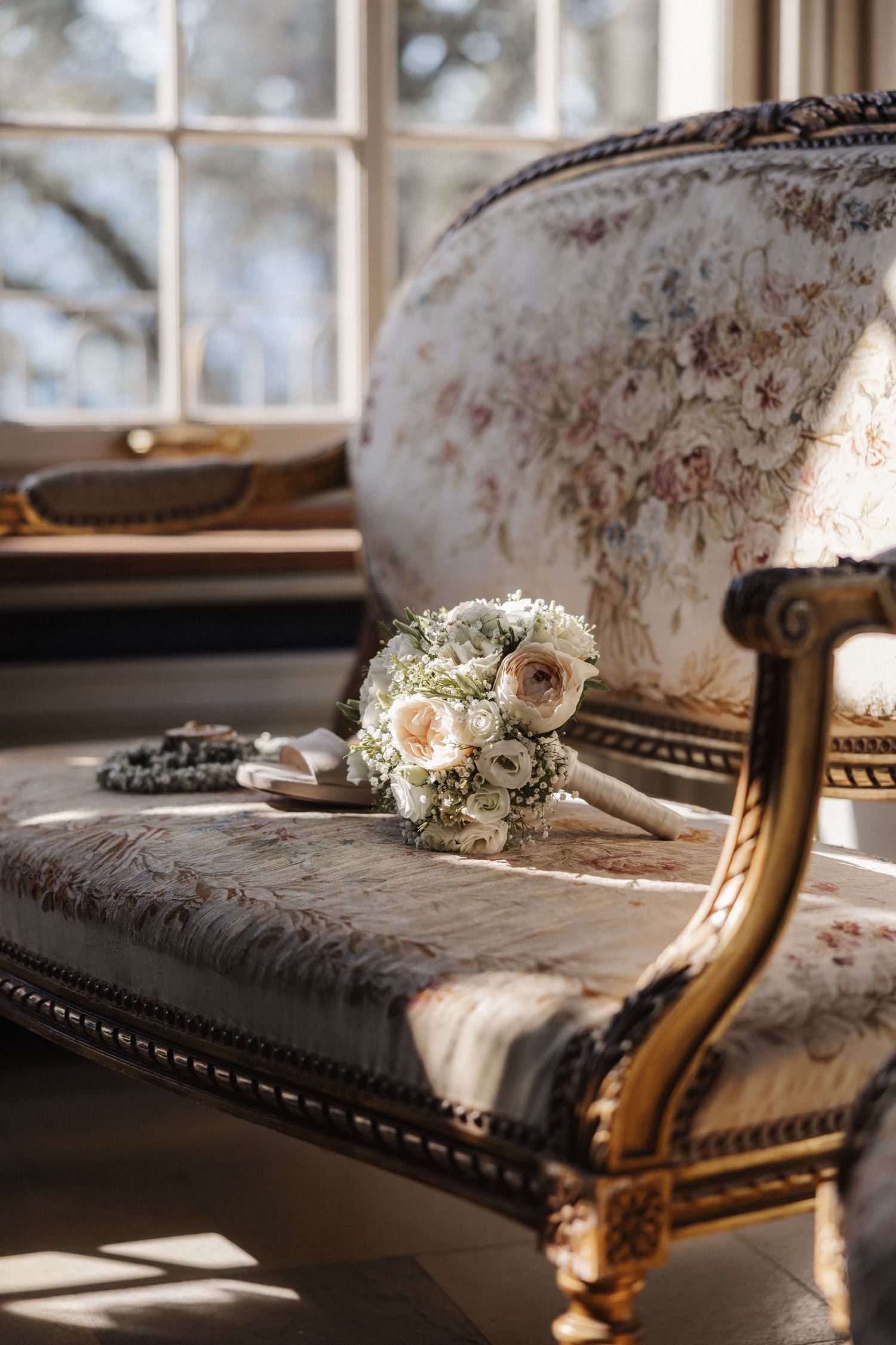 Bridal bouquet of white and blush roses on a vintage floral chaise lounge.