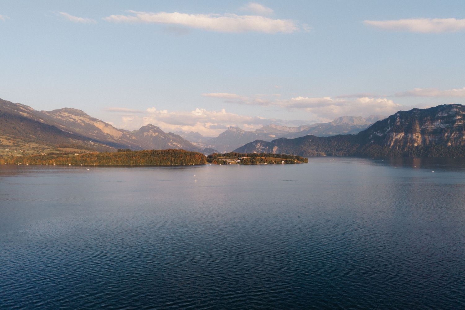 Serene aerial view of a calm alpine lake surrounded by mountains and a small forested peninsula.