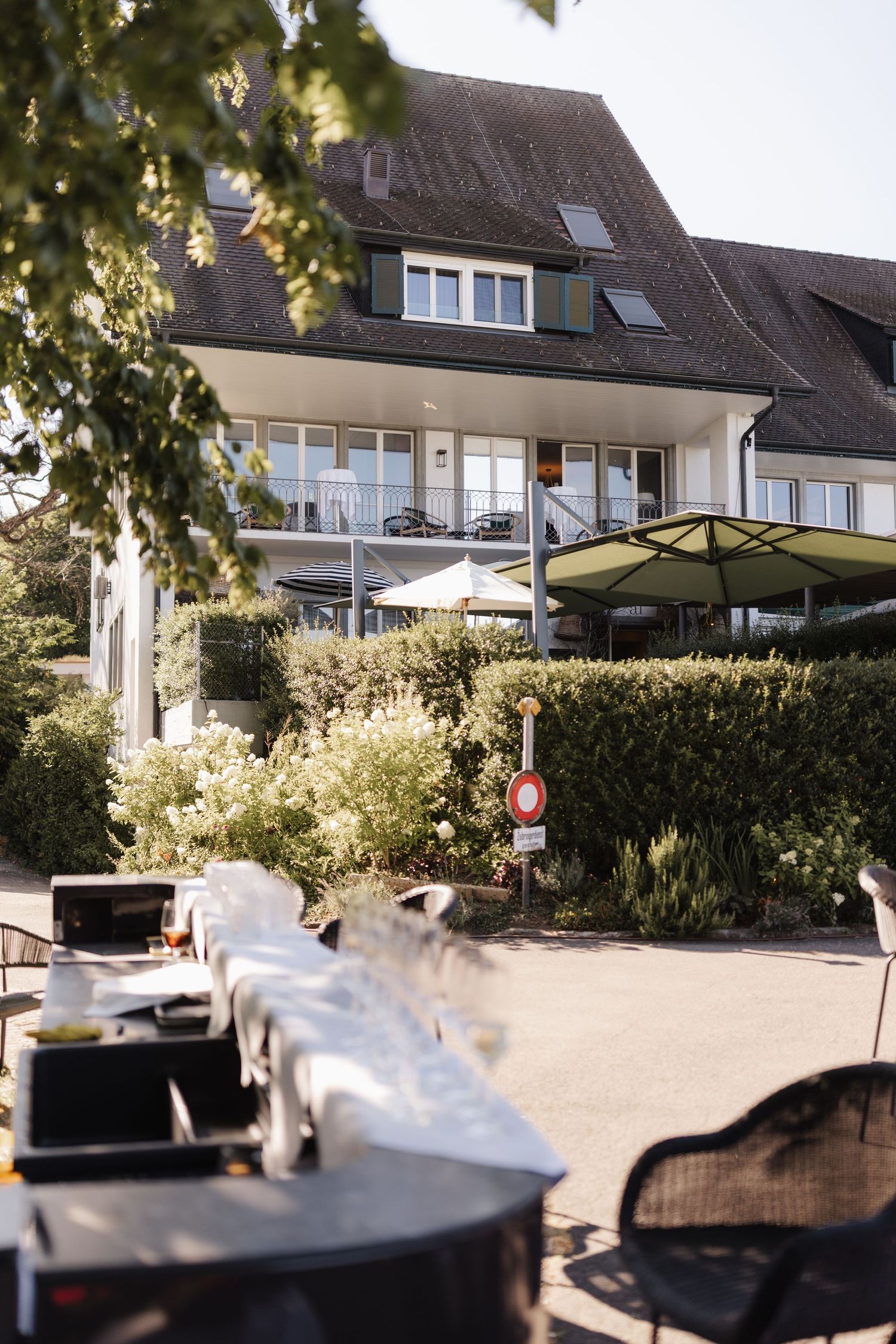 Elegant white European hotel building surrounded by lush green hedges and gardens on a sunny day.