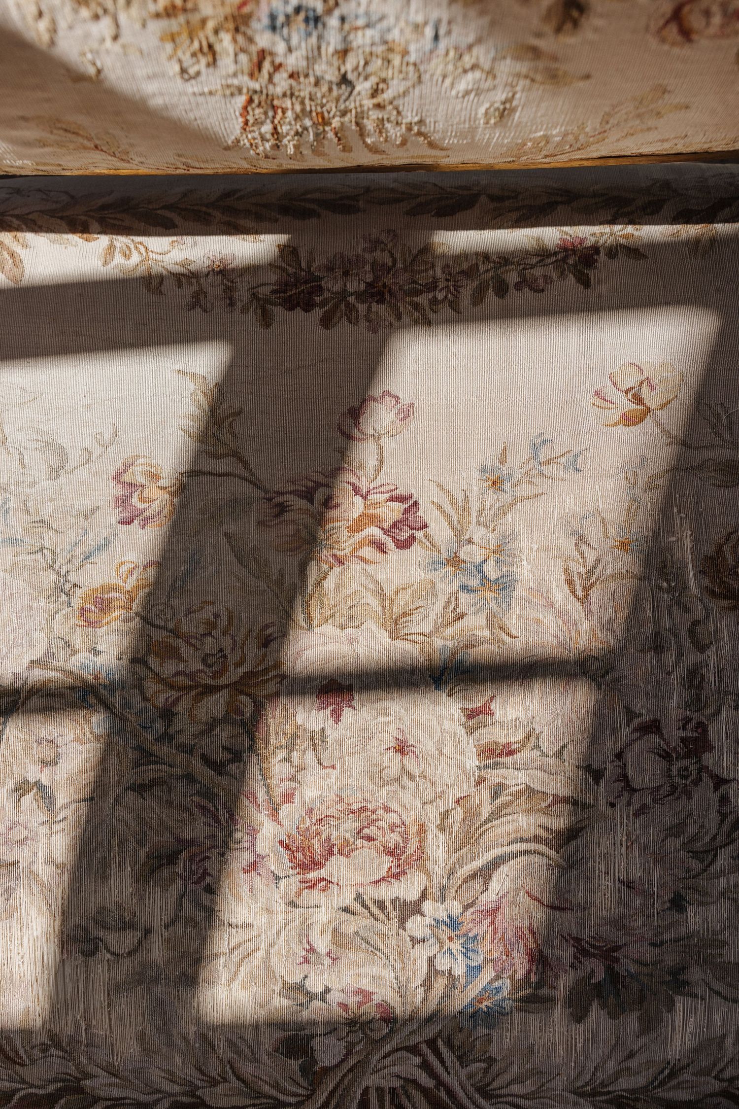 Sunlight casting geometric shadows across a vintage floral tapestry fabric in warm tones.