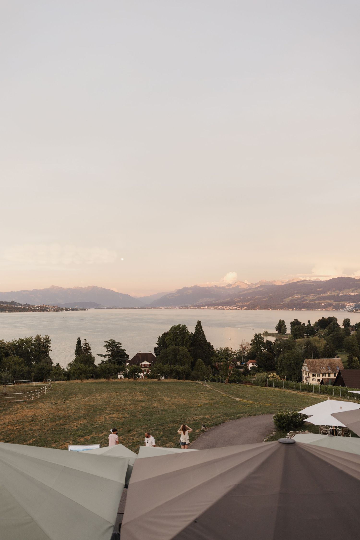Panoramic sunset view of lake and Alps mountains from wedding venue terrace with umbrellas.