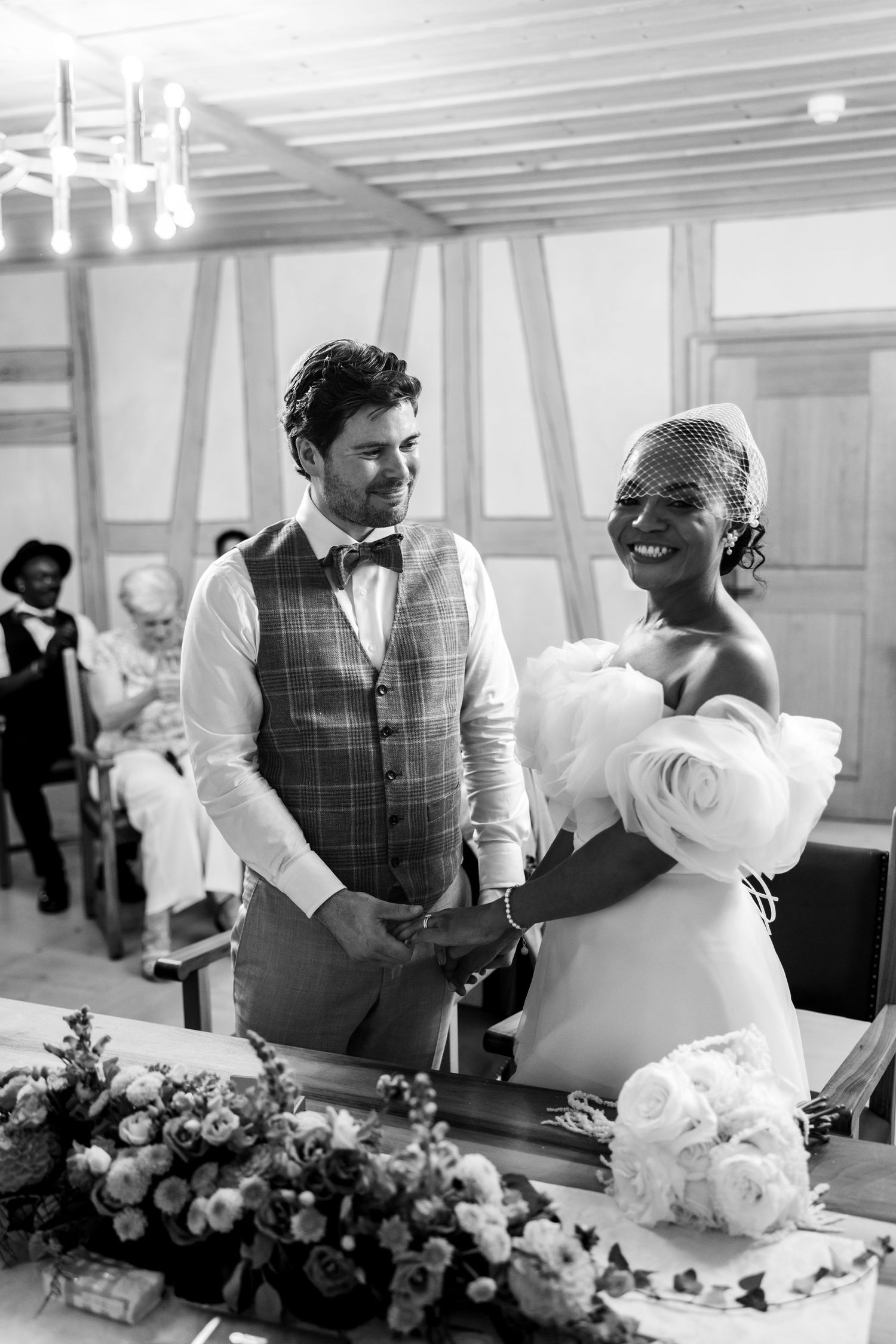 Joyful interracial bride and groom holding hands and smiling at wedding ceremony in black and white.