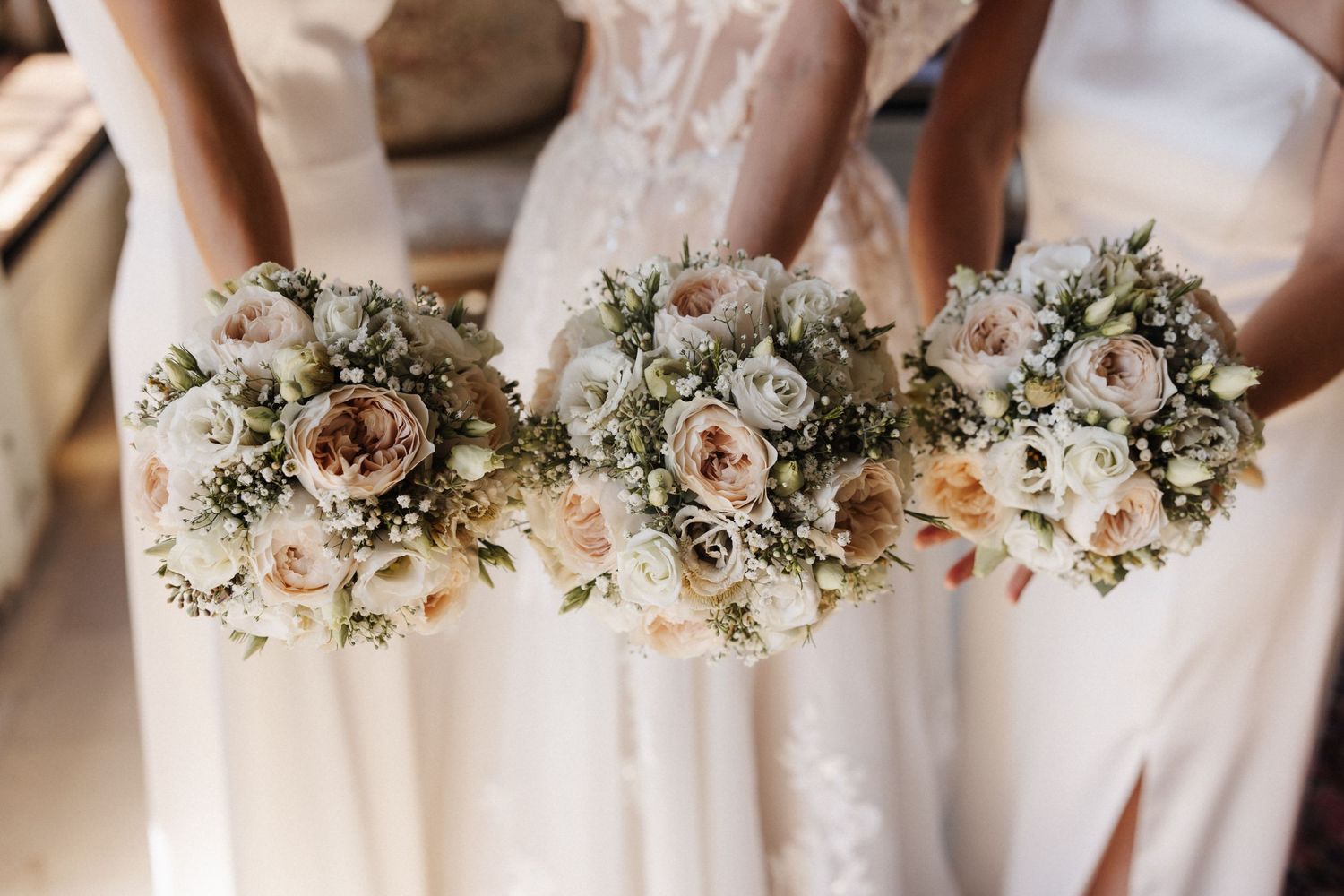 Three bridesmaids holding matching romantic bouquets of white and blush roses with gypsophila at a wedding.