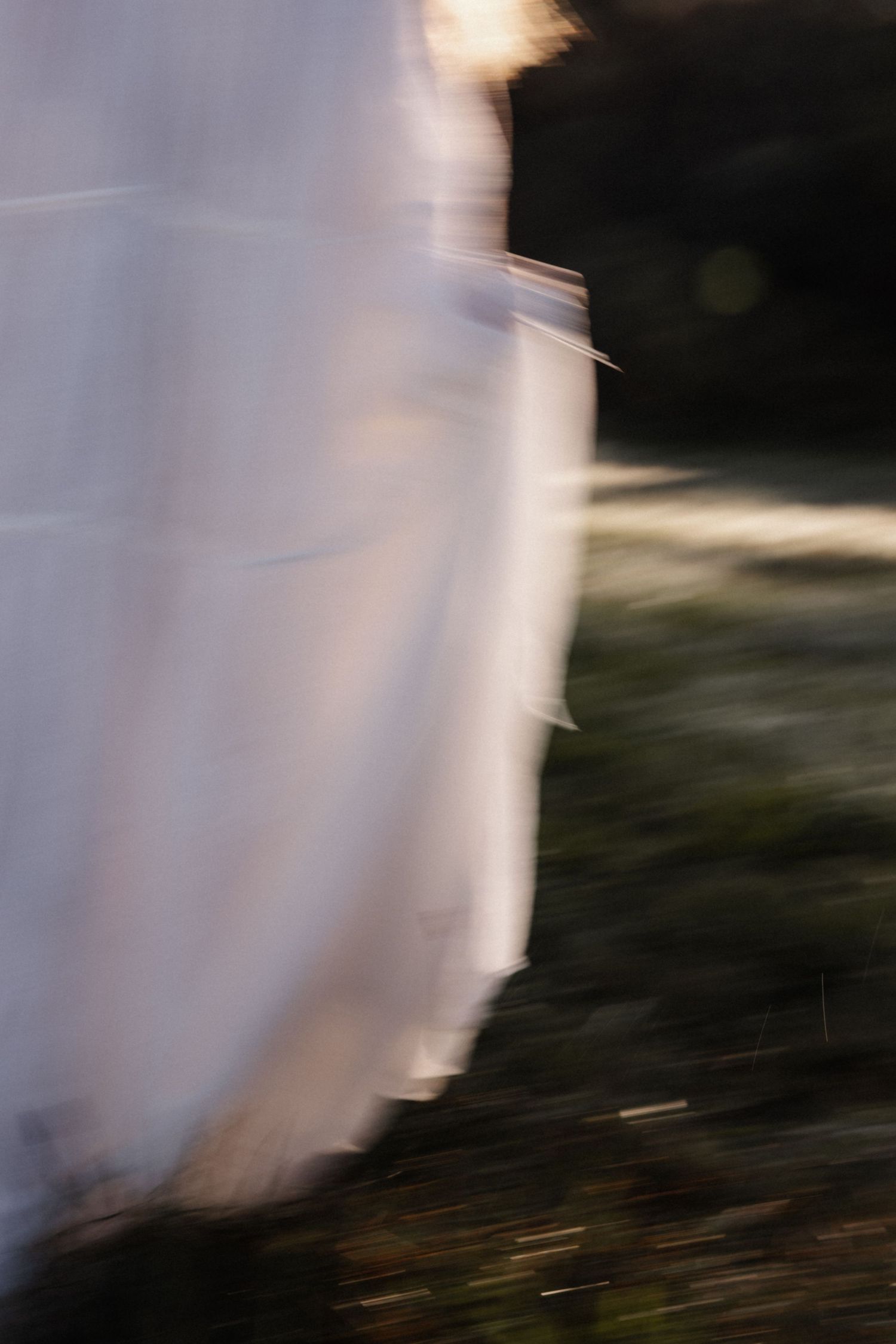 Abstract motion blur photograph of white fabric moving against a dark natural outdoor background.